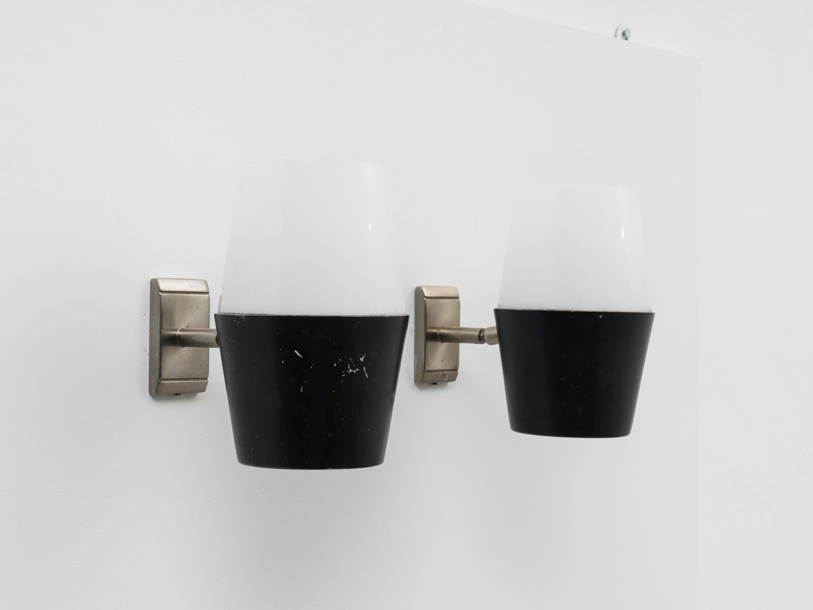 Cette paire d'appliques articulées noires et blanches a été conçue et fabriquée par Stilux Milano au début des années 1960.
Depuis le milieu des années 1950, Stilux Milano est l'un des principaux fabricants italiens de luminaires, avec Stilnovo,