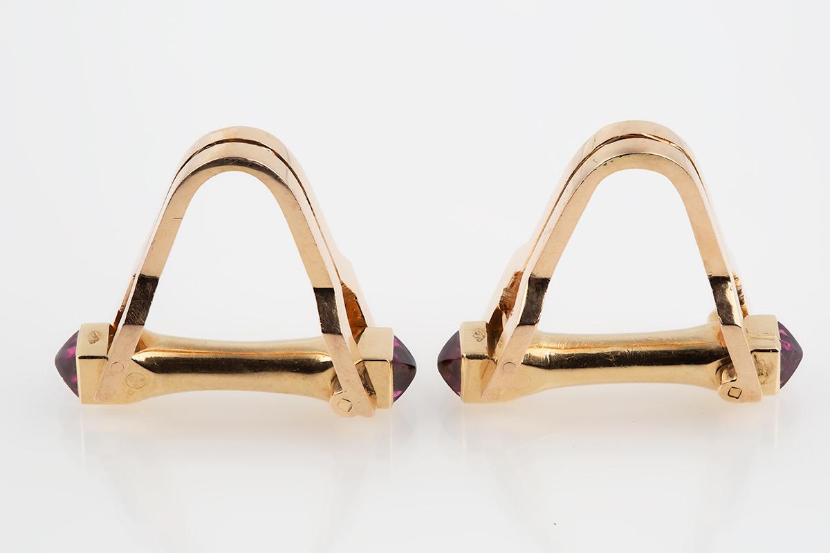 A heavy quality pair of equestrian stirrup shaped cufflinks in 18 karat yellow gold. The opening bar on each link is set with two cabochon rubies, one at either end. These 1950’s vintage cufflinks are designed to be worn around the cuff with the bar