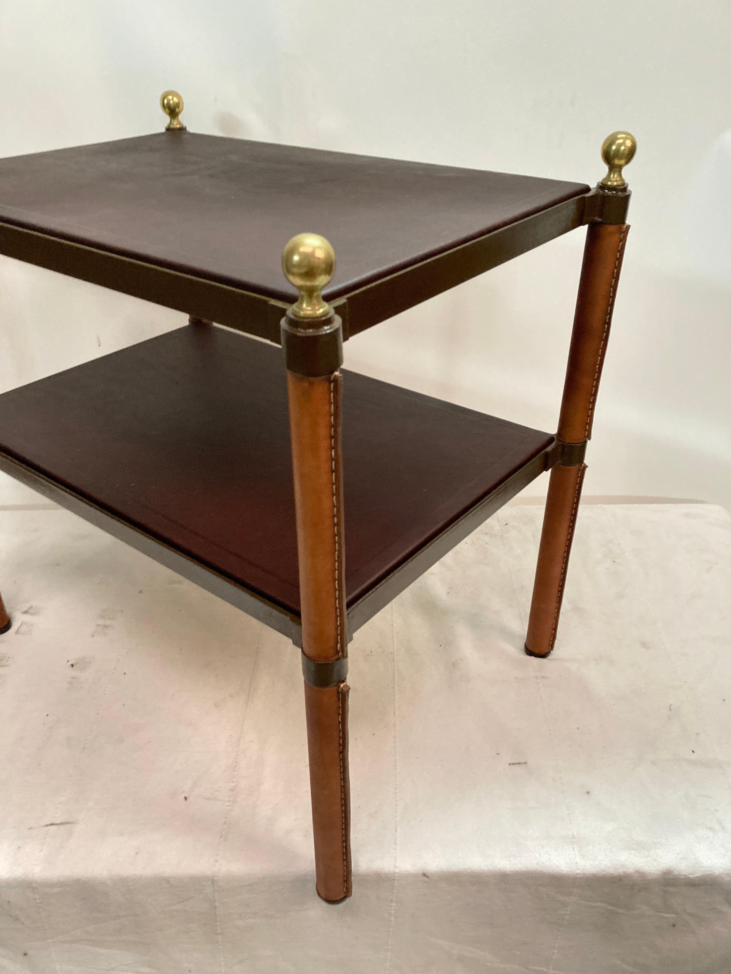 Paire de tables d'appoint en cuir surpiqué des années 1950.
2 niveaux recouverts de cuir chocolat 
Boules de bronze à chaque coin
Grood condition
