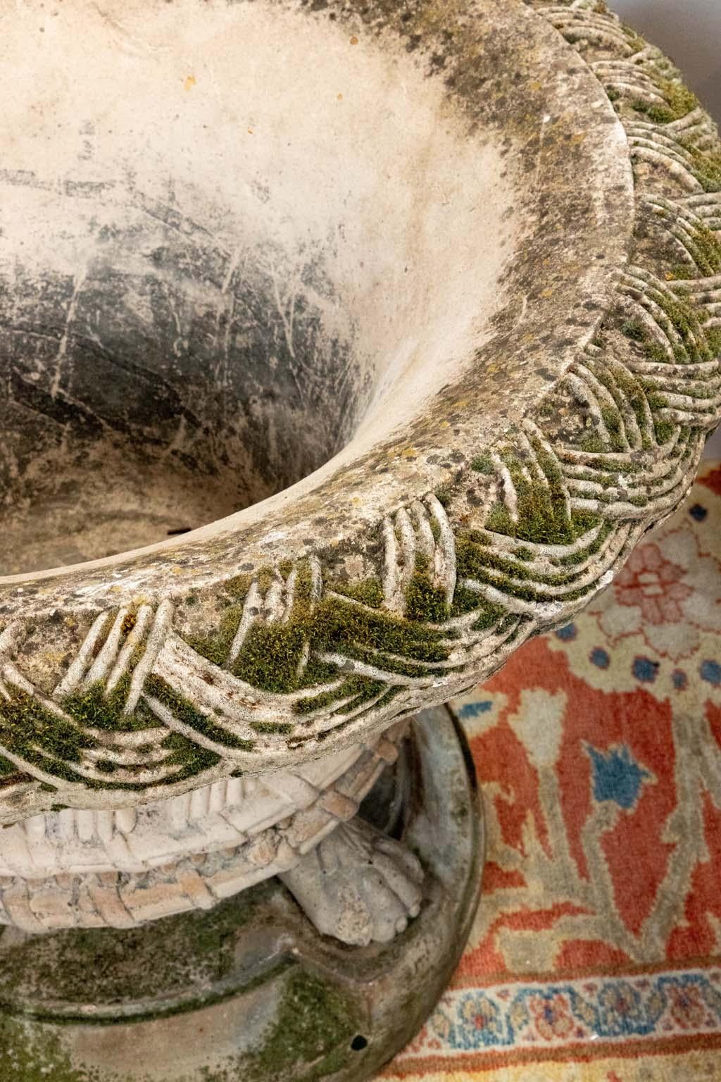 Pair of mid 20th century cast and patinated stone urns with a basket weave design sitting on a clawfoot base. 
