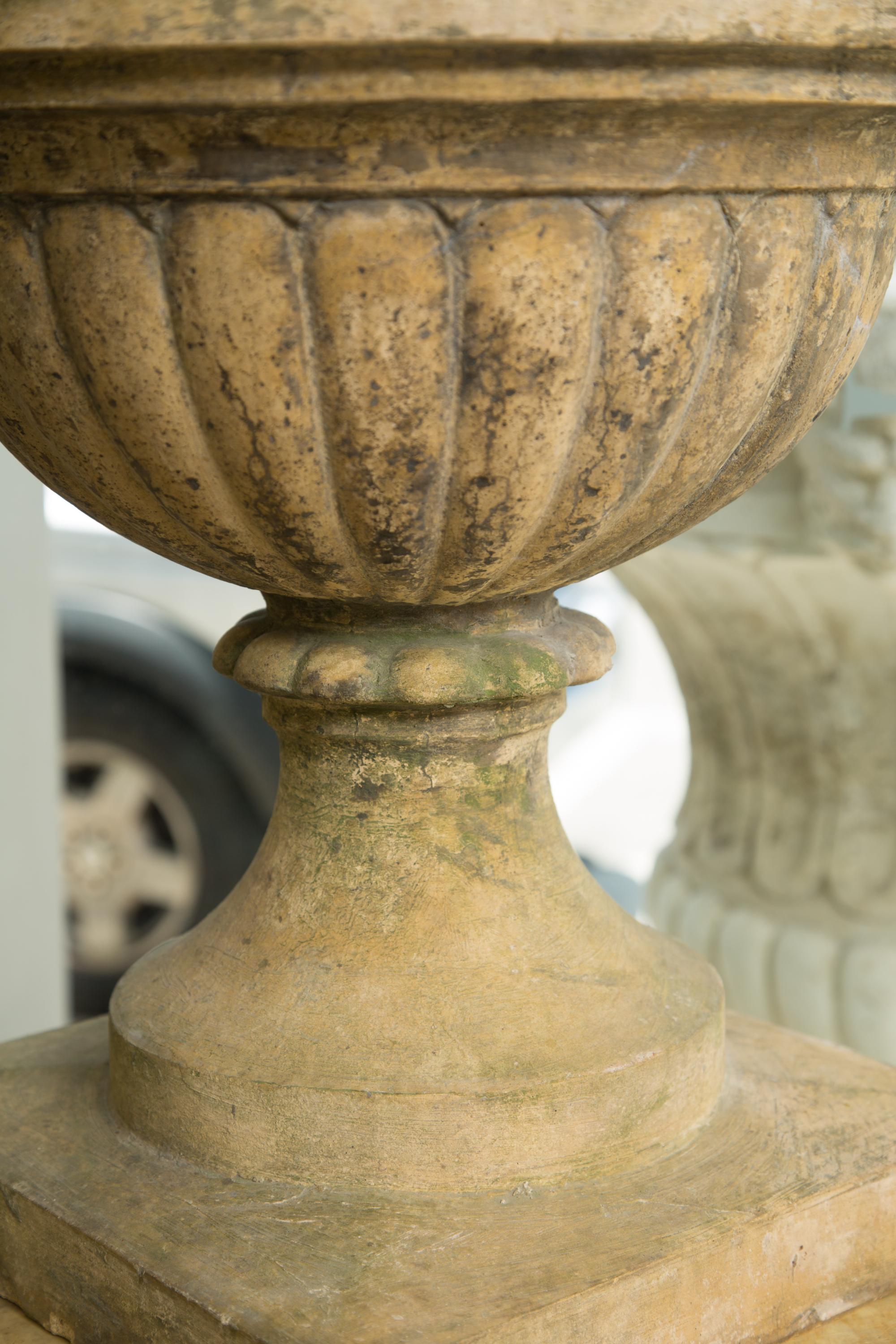 This is a stunning and stately pair of neoclassical early 20th century English cast stone urns. The 19th century urns are placed on later custom faux marble pedestals.