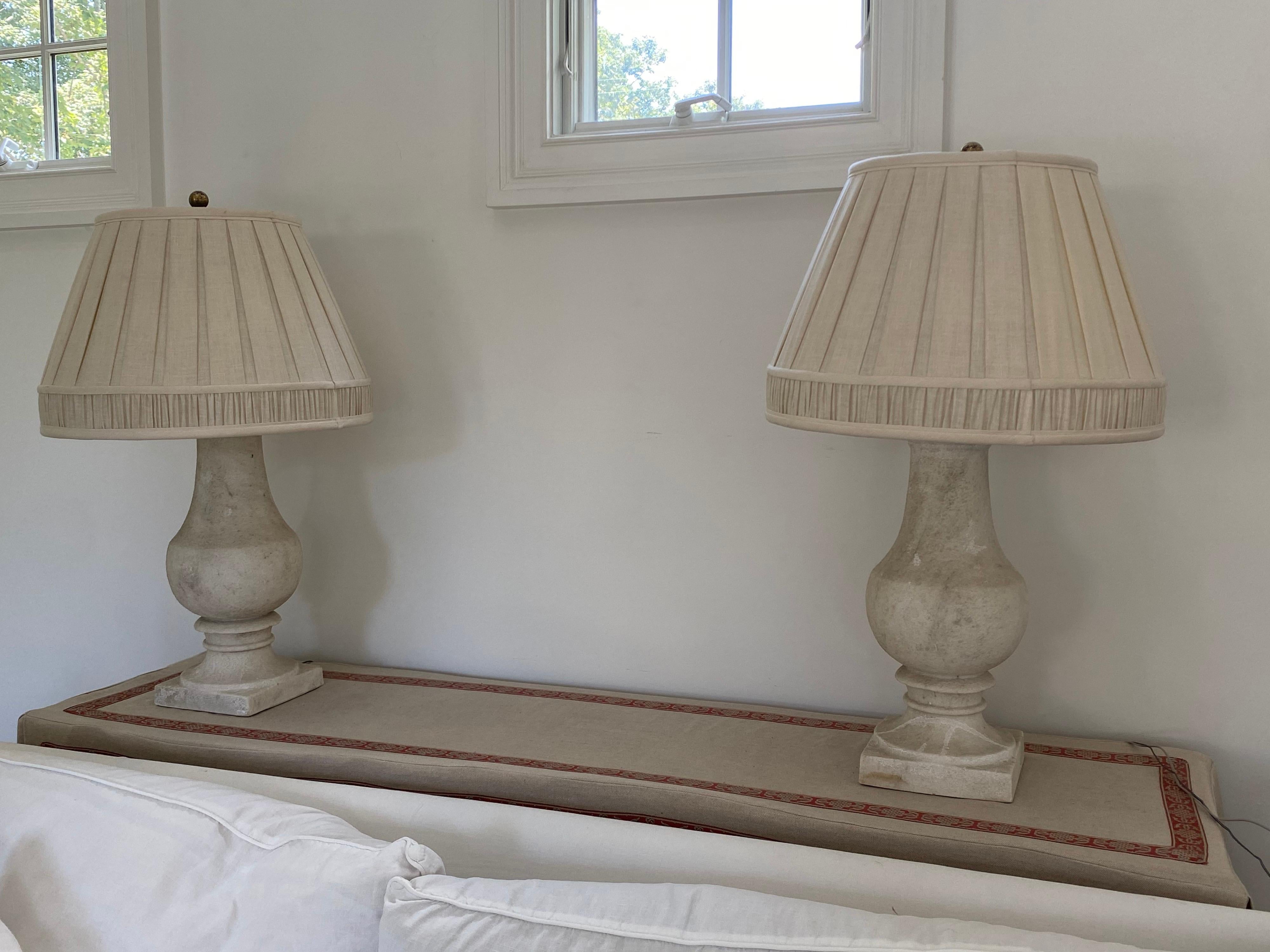 Pair of stone lamps, late 20th century, 
Classic shape in solid stone form. Sold with pleated shades unless otherwise advised. 
Some knicks and wear to stone. Good working, electrified condition. Shades have some fading and general wear. Very
