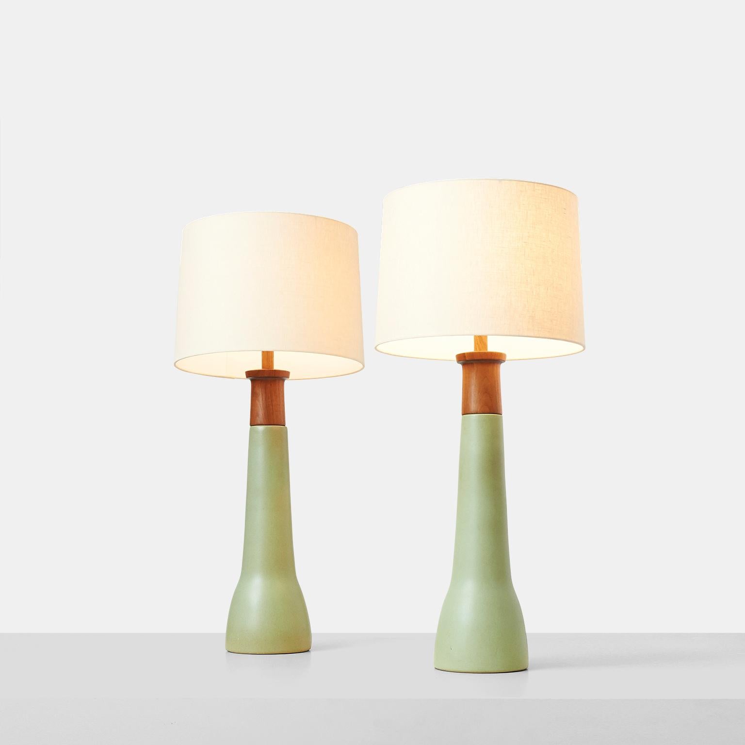A pair of tall stoneware table lamps by Jane & Gordon Martz. The teak turned wood light fitting is affixed to the matte light green stoneware base. Both lamps include the harp and teak finial. Etched “martz” on the back.

Shades not included. New