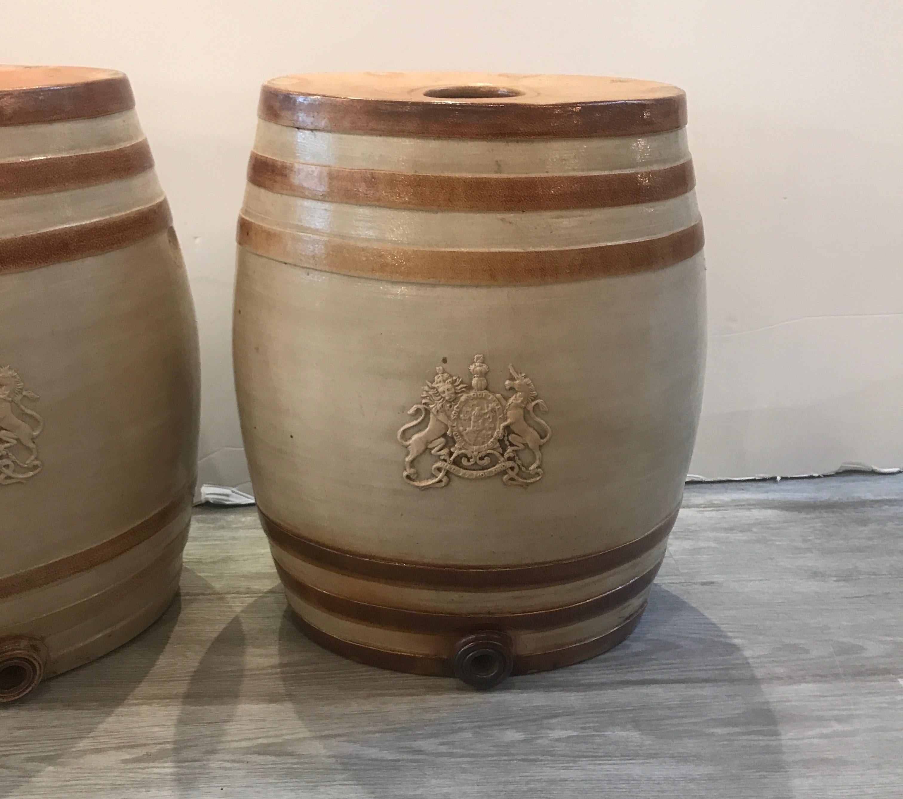 A remarkable pair of English stoneware wine kegs with the armorial seal. The large oval barrel shape with crest on front with opening at the bottom for a spigot (not available). The salt glazed surface in a light tan with brown decorative banding.