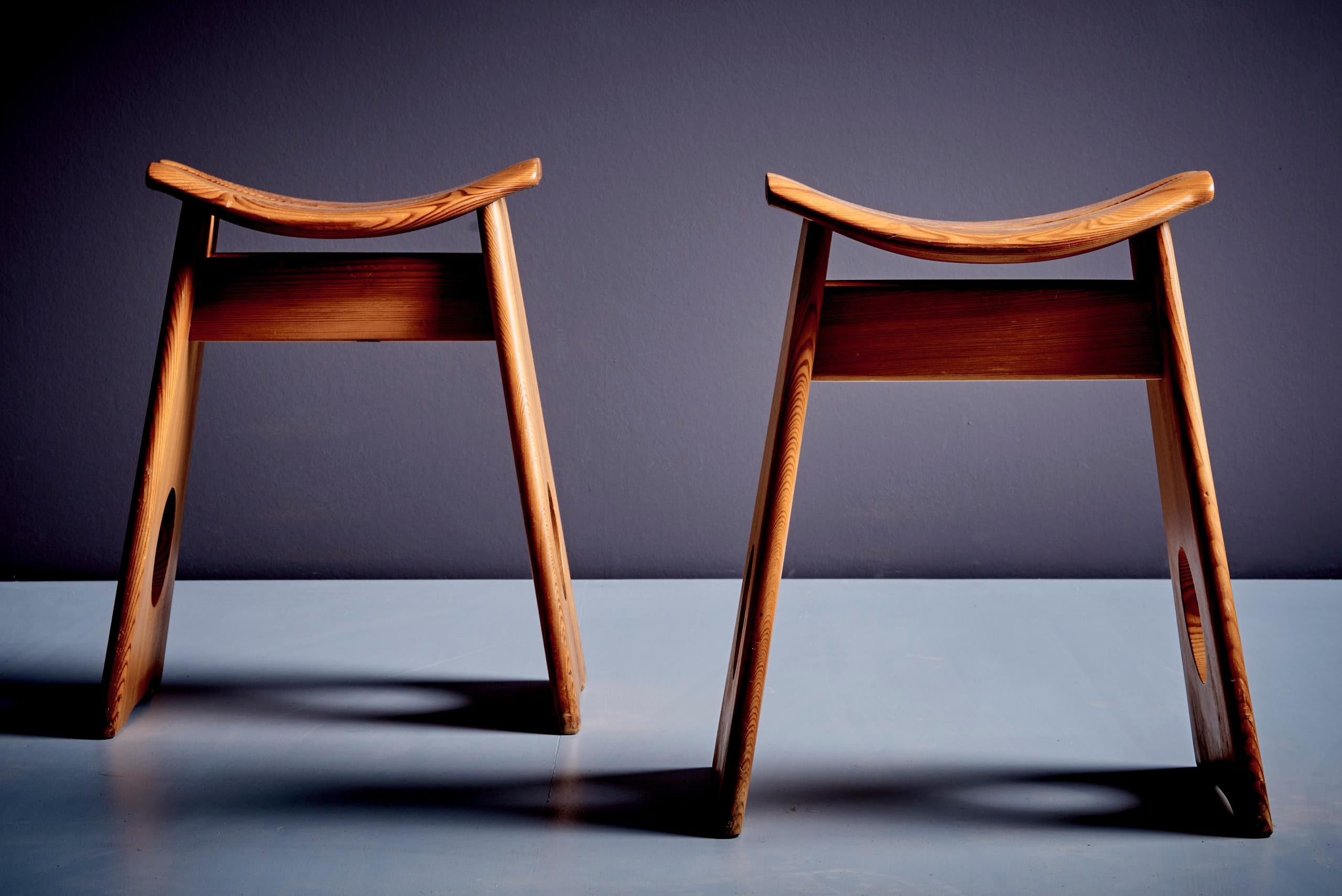 Bold pine stools by Gilbert Marklund, featuring a contoured saddle seat that highlights the expressive wood grain. A-frame legs with circular cutouts complete the sculptural silhouette. A standout example of Scandinavian Brutalist design. Vintage