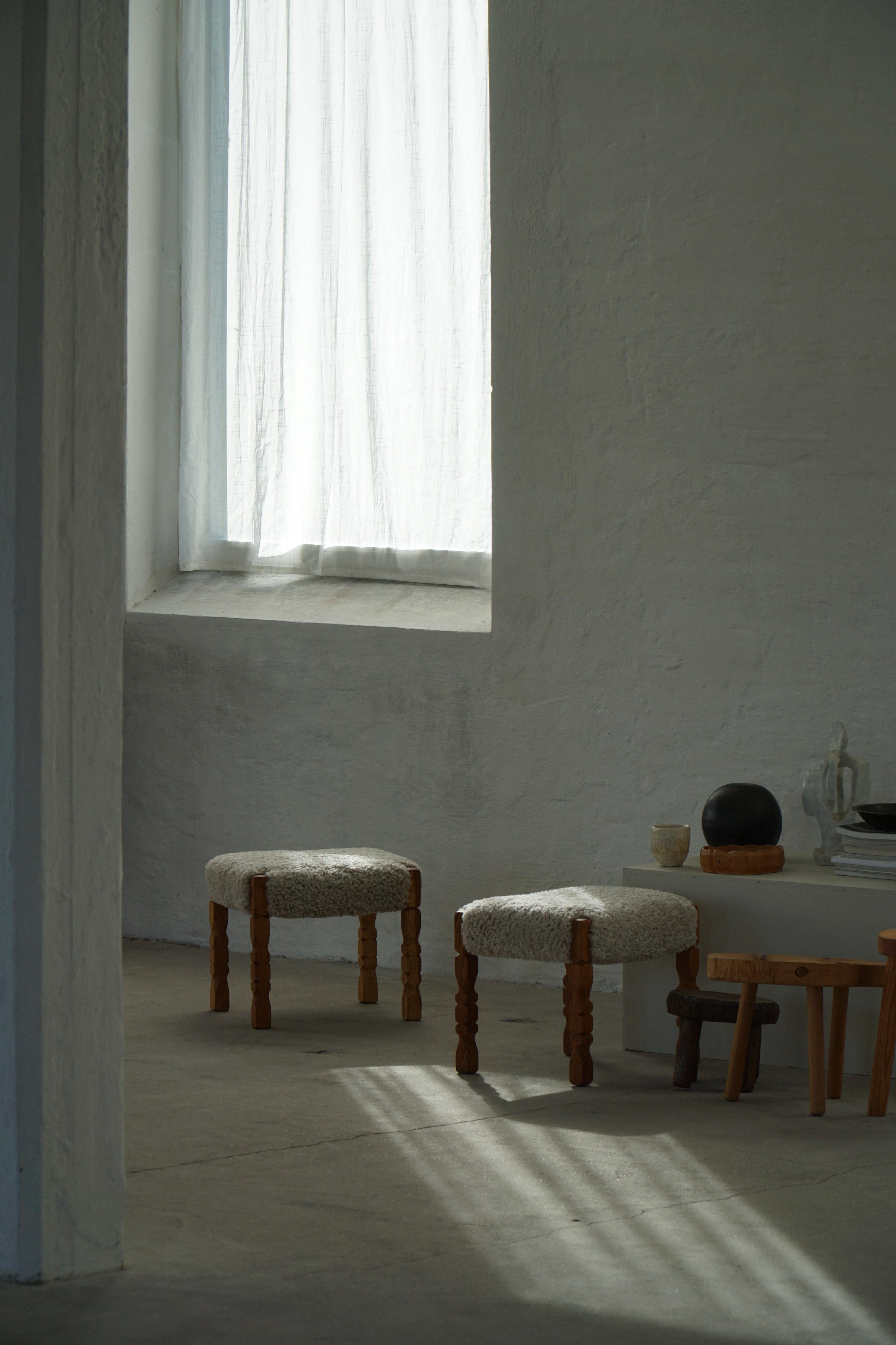 Paire de tabourets, poufs ou ottomans en chêne massif de belle facture, chacun doté d'une assise généreusement rembourrée en laine d'agneau douce et naturelle. Fabriqué dans le style de Henning Kjærnulf dans les années 1950. Ces pièces illustrent le