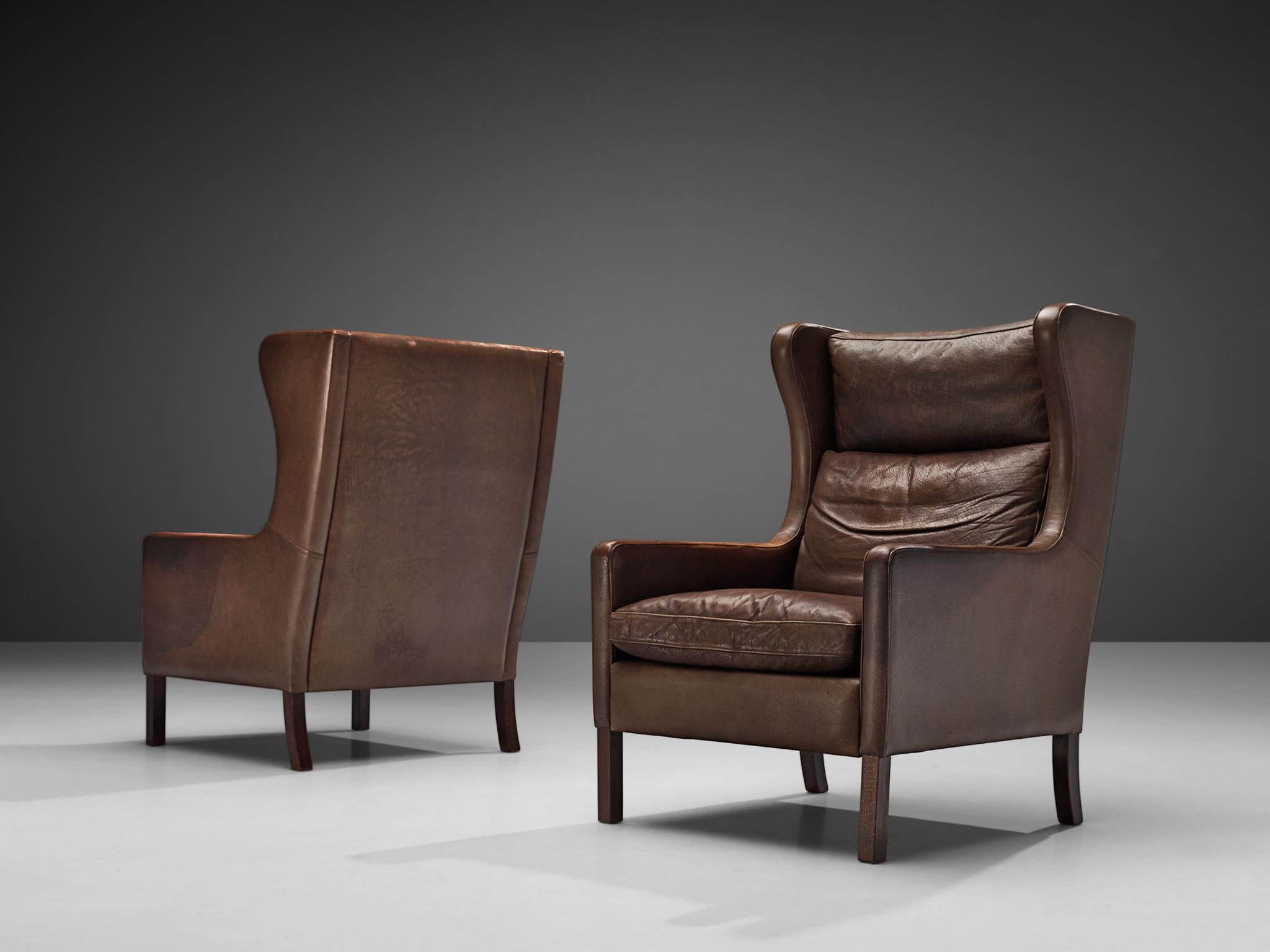 Stouby Denmark, pair of lounge chairs, leather, Denmark, 1940s
 
Danish wingback lounge chair in the style of Frits Henningsen (1889-1965). Both chairs are upholstered in a dark brown leather that shows admirable patina. The design is