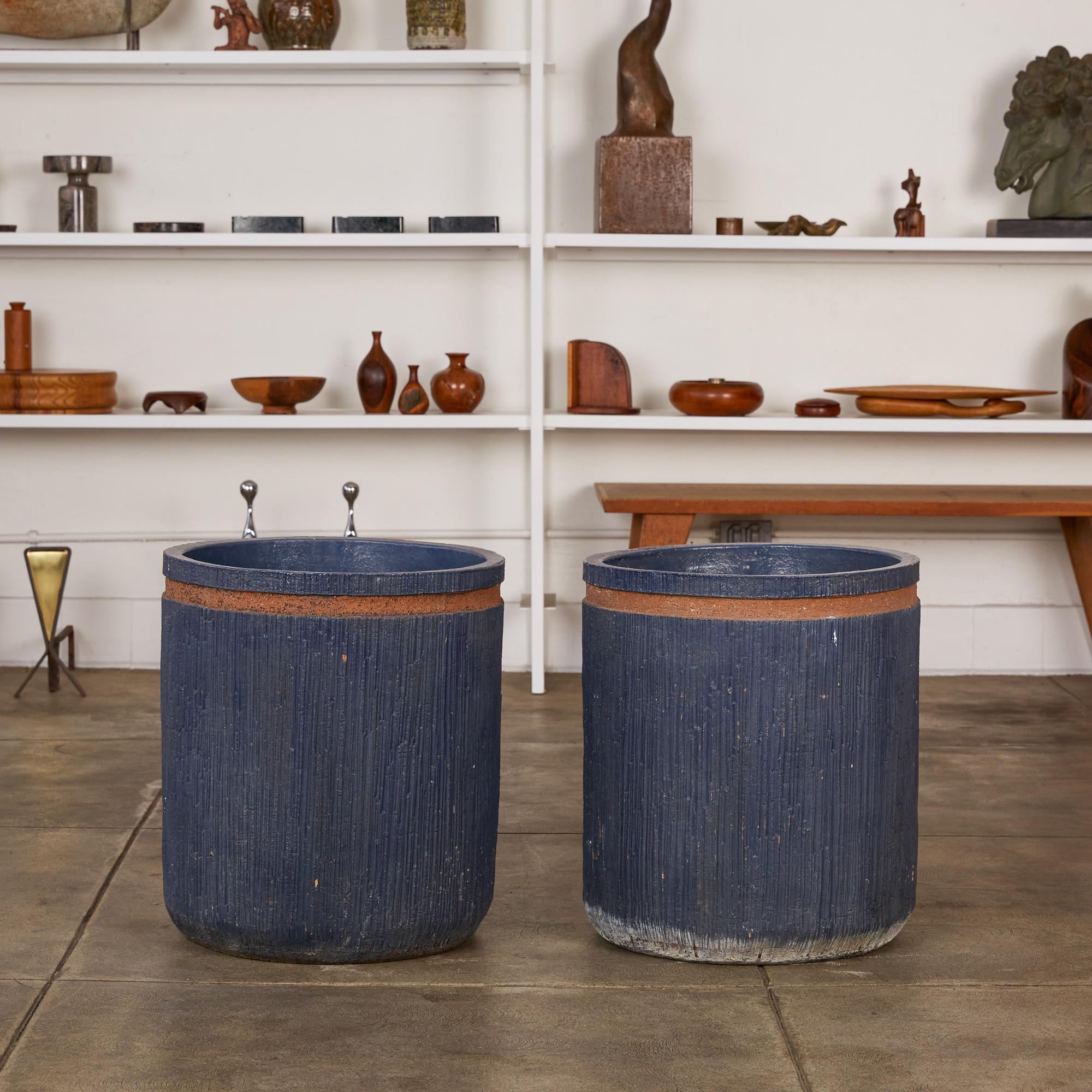A pair of studio ceramic stoneware planters, c.1982. The stoneware planters are covered in an indigo colored glazed on the interior and exterior of the planter. The exterior is incised with a vertical striation and has a horizontal inset stripe that