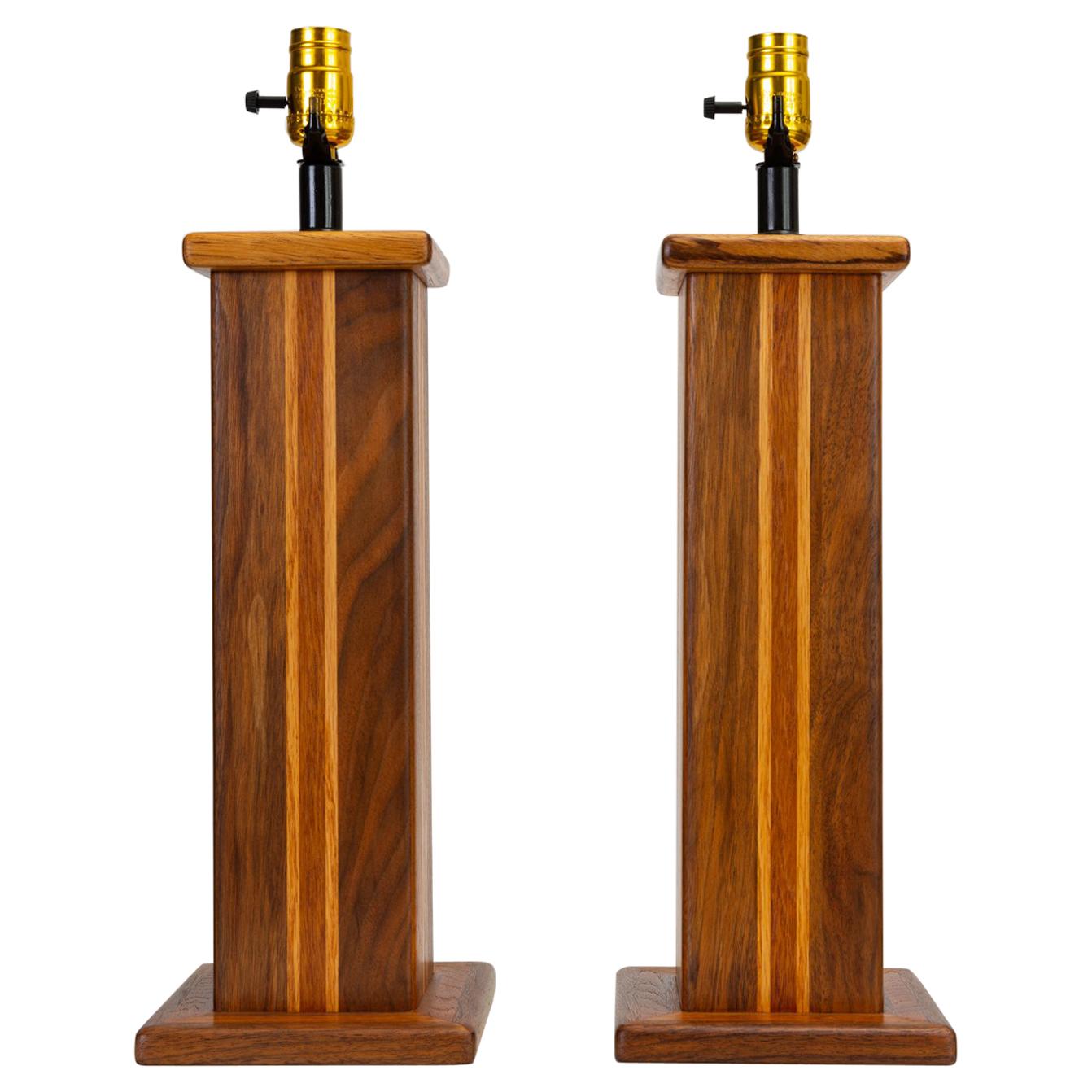 A pair of American handcrafted wooden pedestal lamps, having a columnar body in solid walnut, inlaid with oak and African mahogany, capped by a square base of walnut and mahogany and a capital in nicely figured zebrawood.  A small portion of the