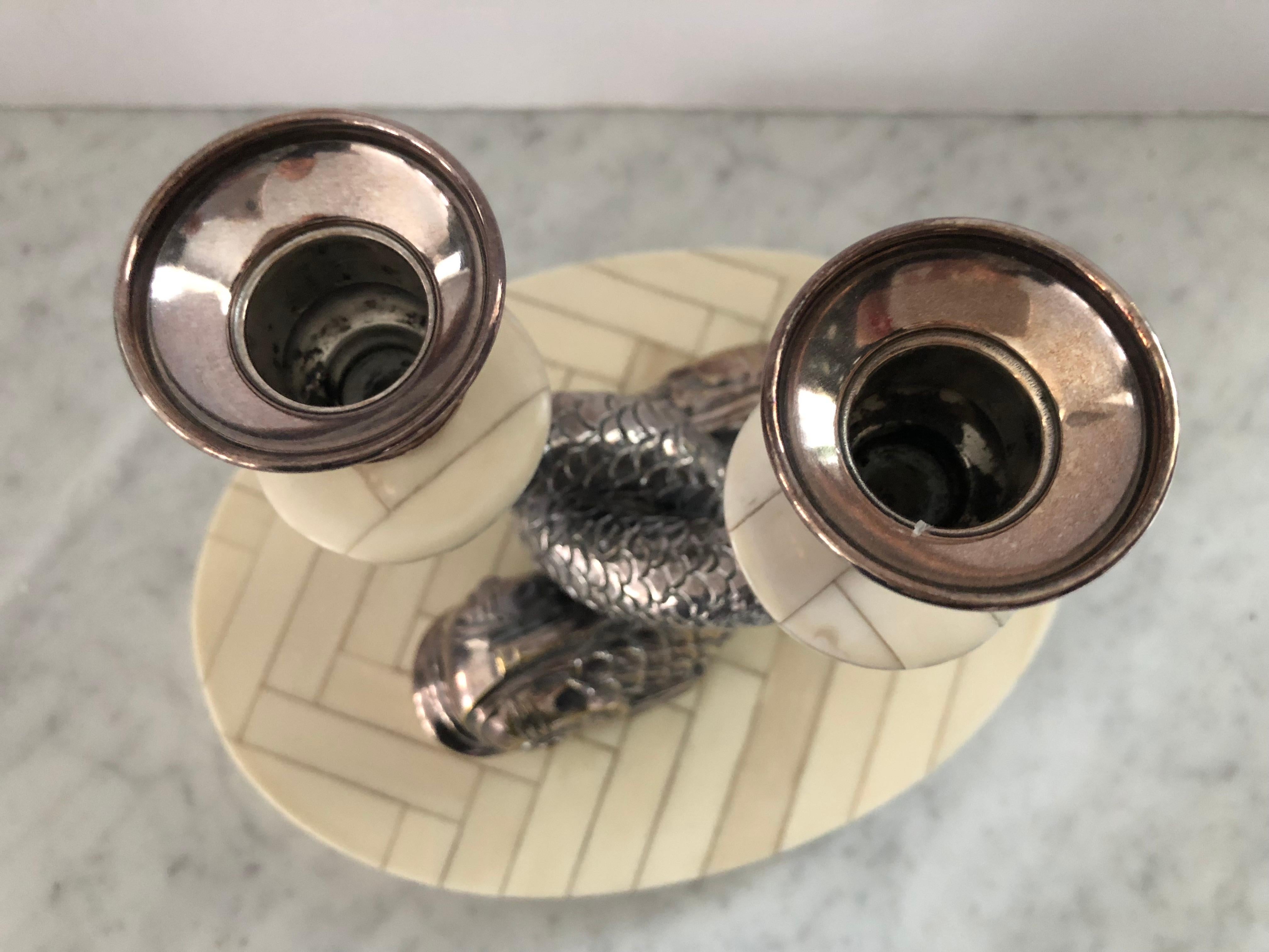 Fabulous pair of midcentury entwined dolphin candlesticks in silver plate by Anthony Redmile (UK). Known for his unique tabletop creations, these candlesticks are on oval tessellated bone bases. One candlestick has a small bend in the candle cup and