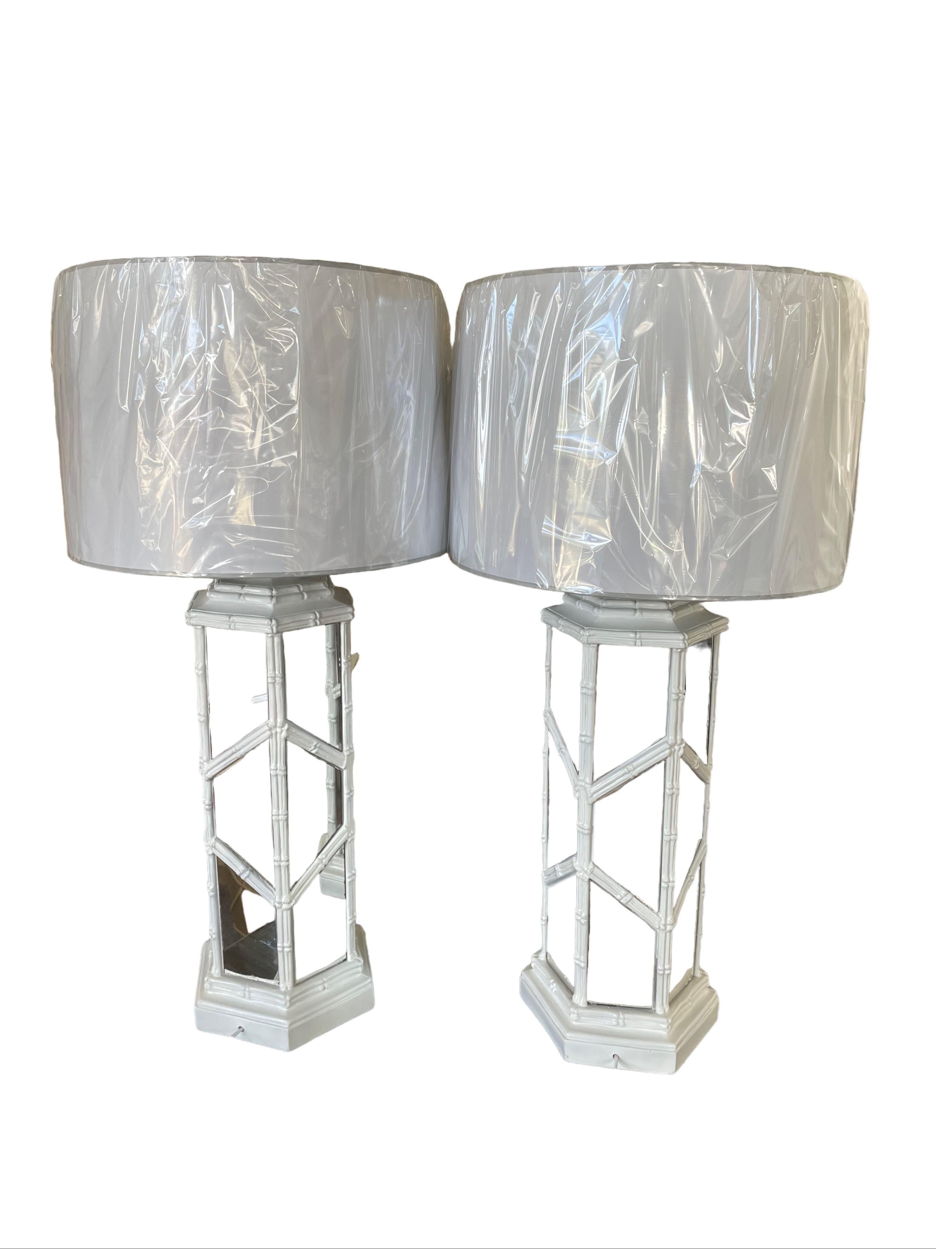 A stunning pair of vintage lamps boast a distinctive combination of faux bamboo and mirrored inlay. The classic crisscross bamboo design in white sets off the many mirrored inlaid sections thus enhancing the lamps’ lighting qualities. With classic