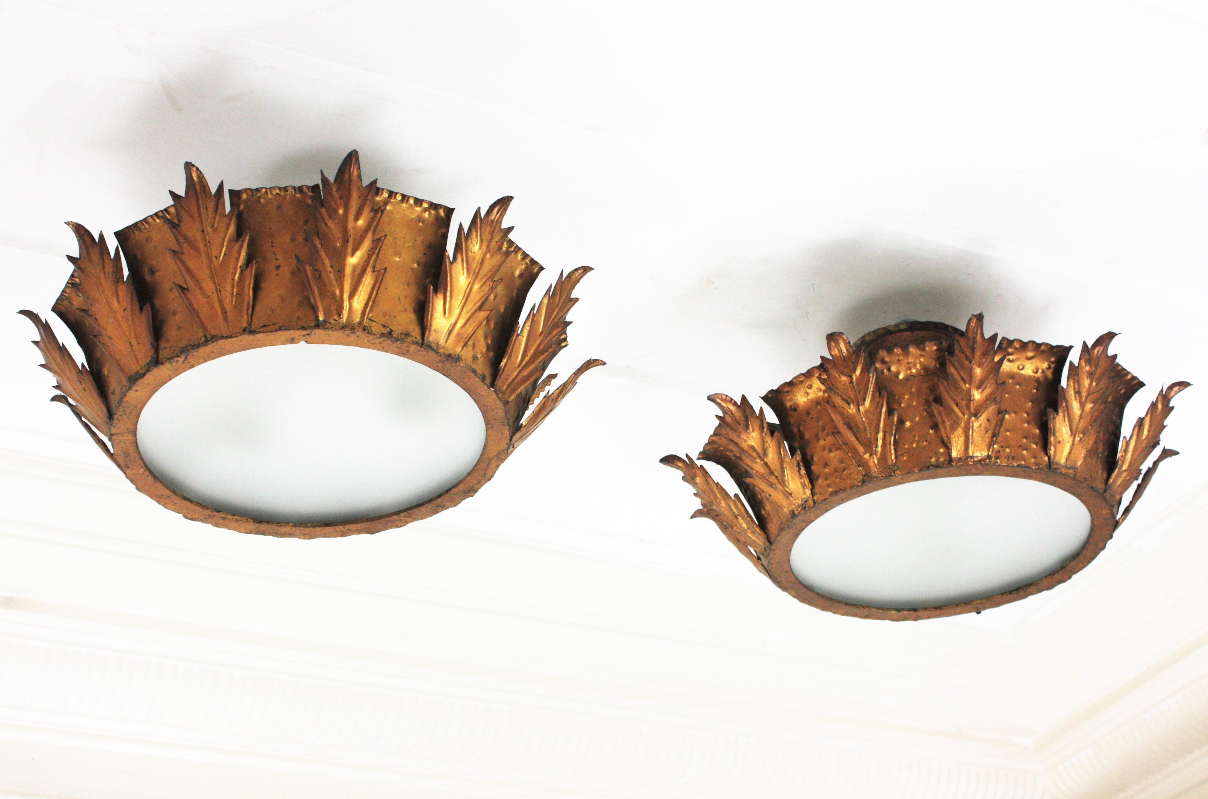 Pair of Sunburst crown flush mounts, gilt iron, frosted glass, Spain, 1950s.
Beautiful hand-hammered sunburst crown shape leafed flush mount ceiling light fixtures with frosted glass panel diffusers.
This pair of ceiling lights were handcrafted in
