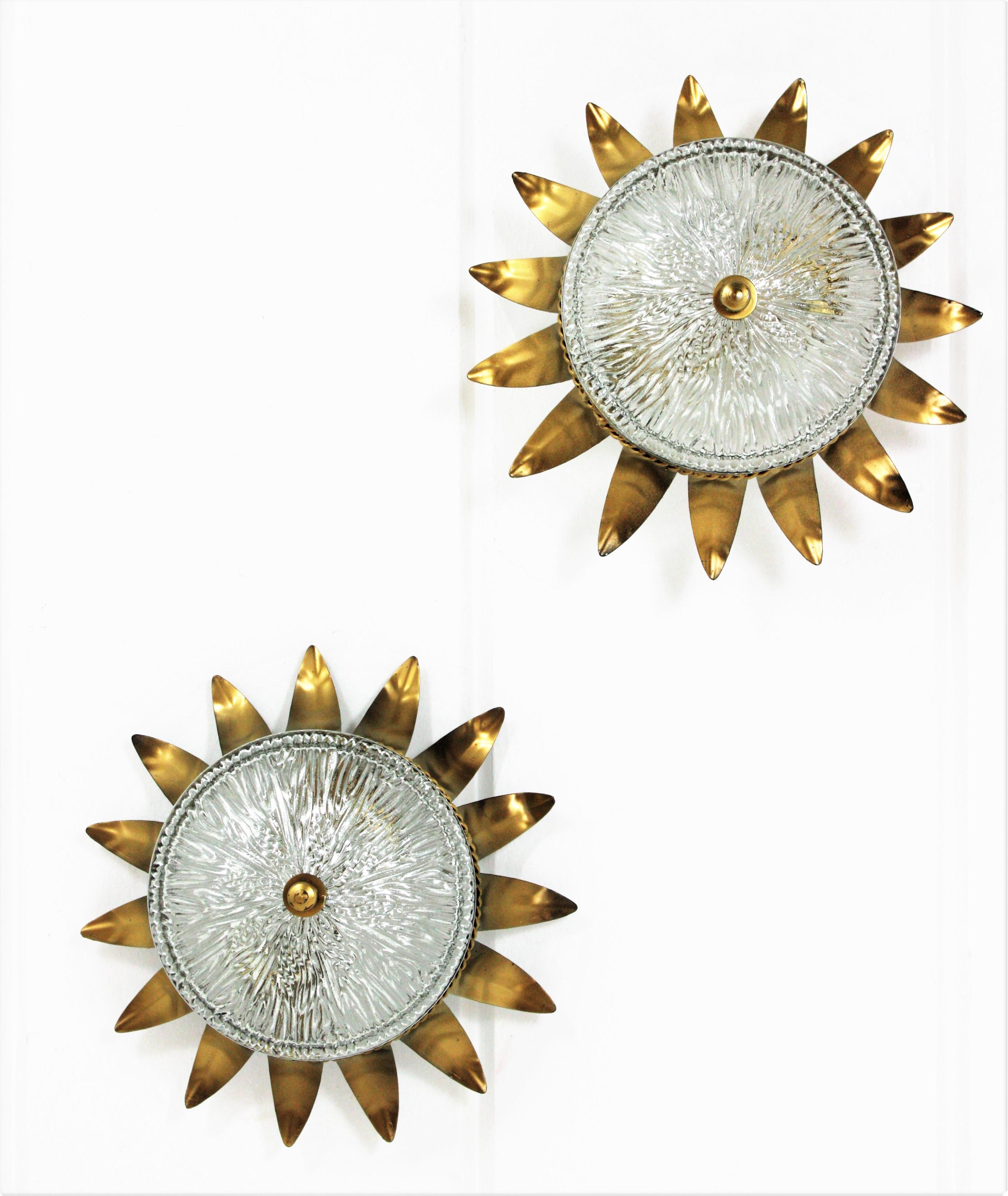 Pair of neoclassical style sunburst ceiling light fixtures from the Mid-Century Modern period, Spain, 1950s.
Both pieces feature a gilt metal sunburst crown shaped structure with a pressed glass shade with a gilt iron finial.
These flush mount