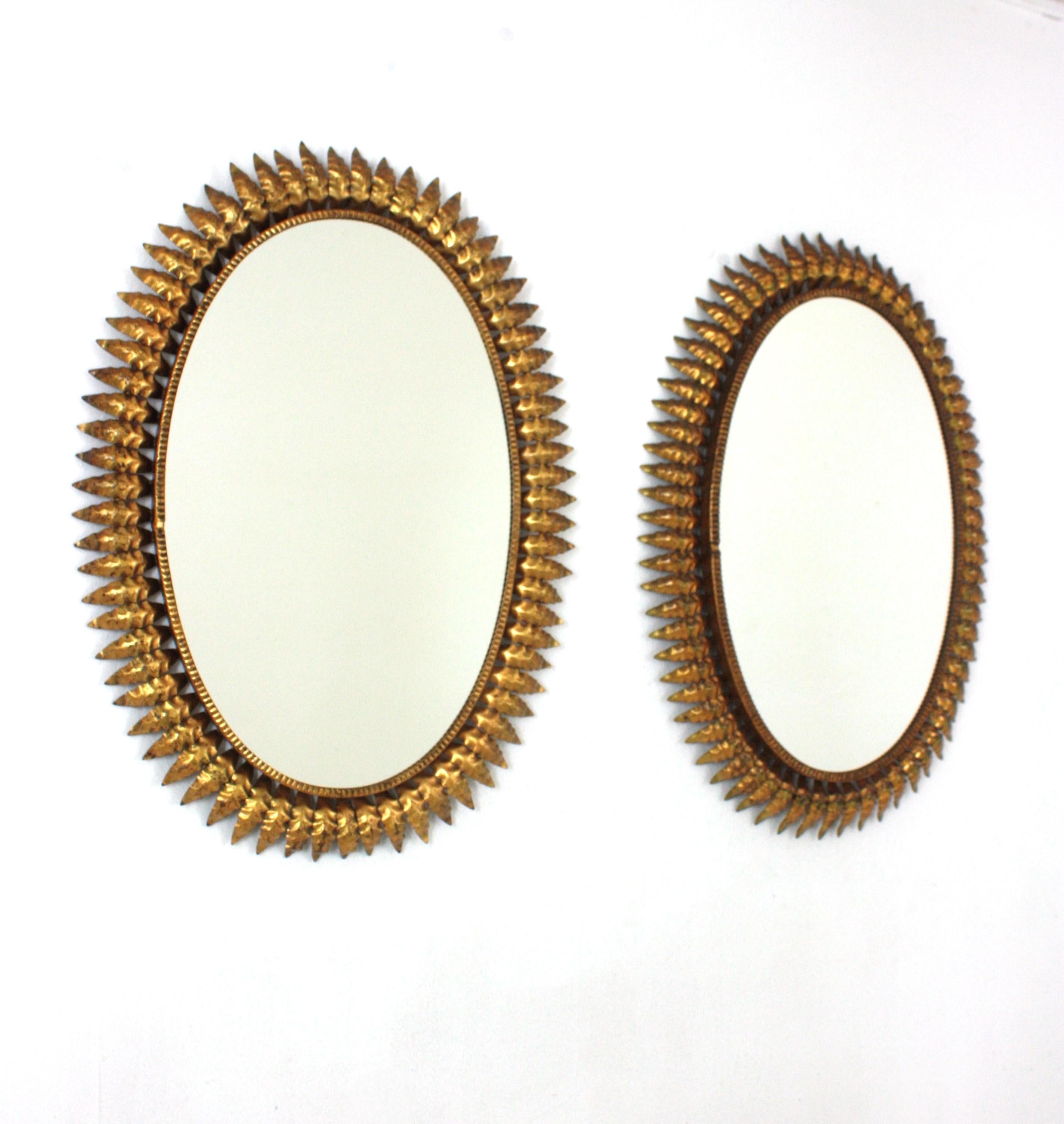 Coppia di specchi da parete ovali a raggiera in ferro della Modernità di metà secolo con cornici a foglia e finitura a foglia d'oro, Spagna, anni Cinquanta.
Questi specchi a foglia di sole altamente decorativi presentano una bella patina che mostra