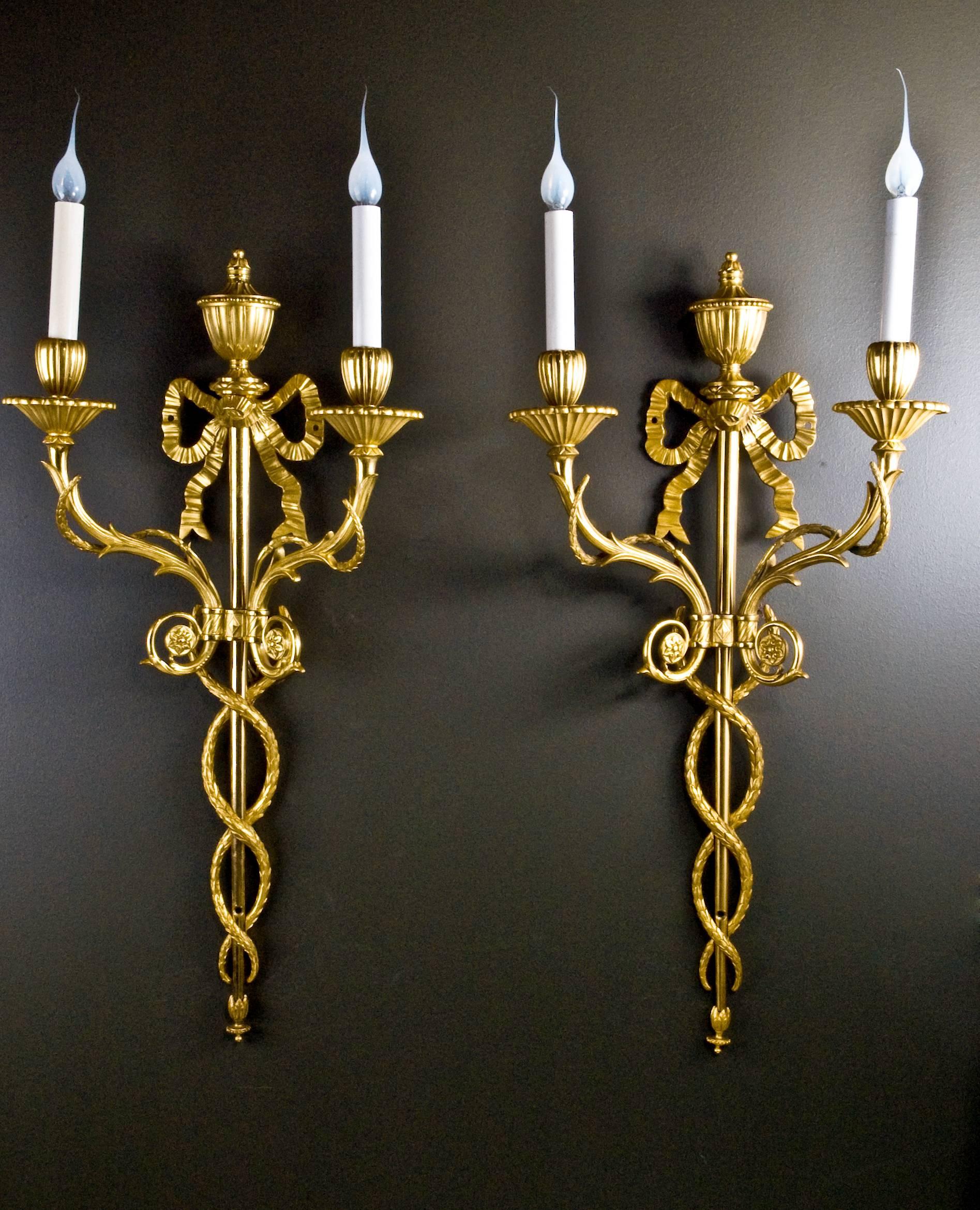 A pair of superb and large antique French Louis XVI style gilt bronze double light wall appliqués of fine quality embellished with a central neoclassical urn and further decorated with a ribbon on the very top.