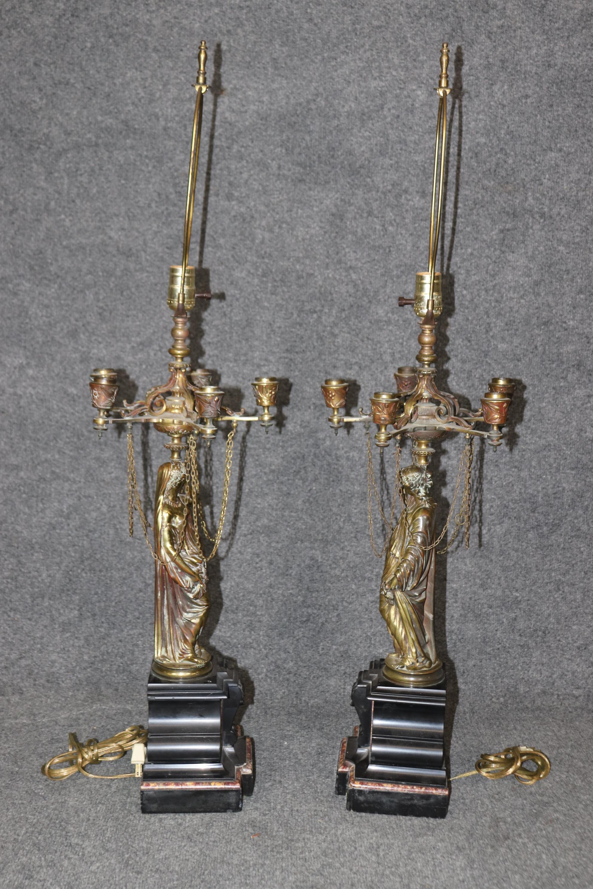 This is a fantastic pair of lamps depicting draped robed women with chains holding up a 5-light array for each lamp. The pair is in good original condition. The pair is perhaps not politically correct, but the quality of the casting and marble base