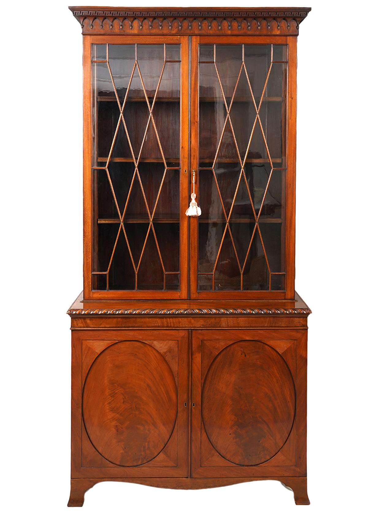 This rare pair of English Edwardian two part bookcases feature finely carved cornices with Greek and Gothic style elements above two doors sporting diamond shaped mountains. The doors open to adjustable shelved interiors. The lower parts feature