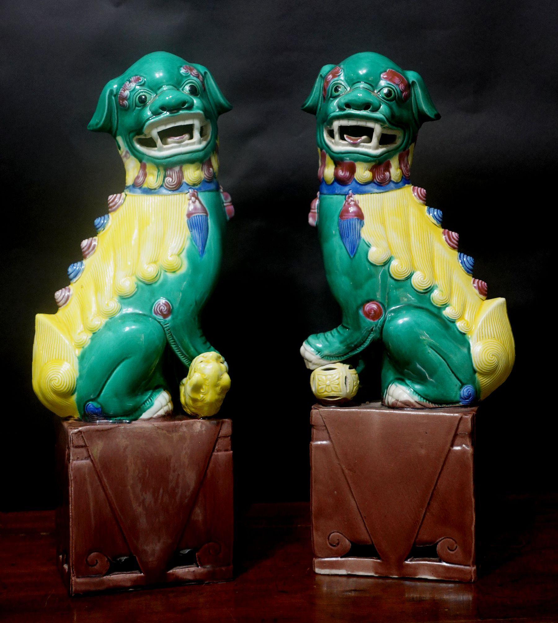 Fine, large, and very detailed pair of Chinese famille verte glazed foo dogs from the early 20th century. The hollow biscuit porcelain figures stand raised on a rectangular base and are looking sideways with open mouths and tongues showing teeth