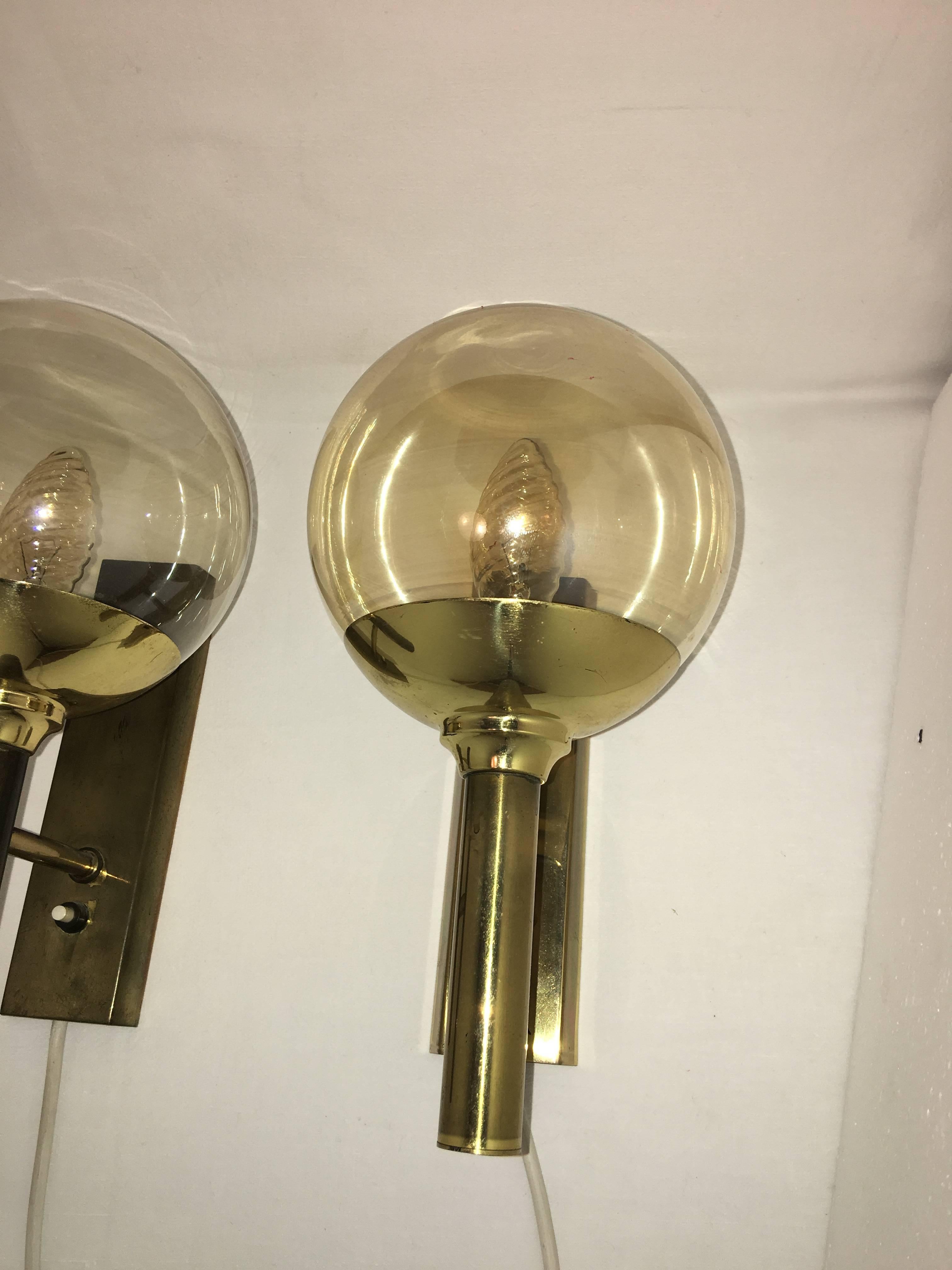 A pair of brass and smoke glass sconces designed by Svend Mejlstrom. Manufactured by Mejlstrom Belysning of Norway. The sconces have a very nice Patina and a 20 inch long cable. Each fixture requires one European E14 candelabra bulb up to 40 watts.