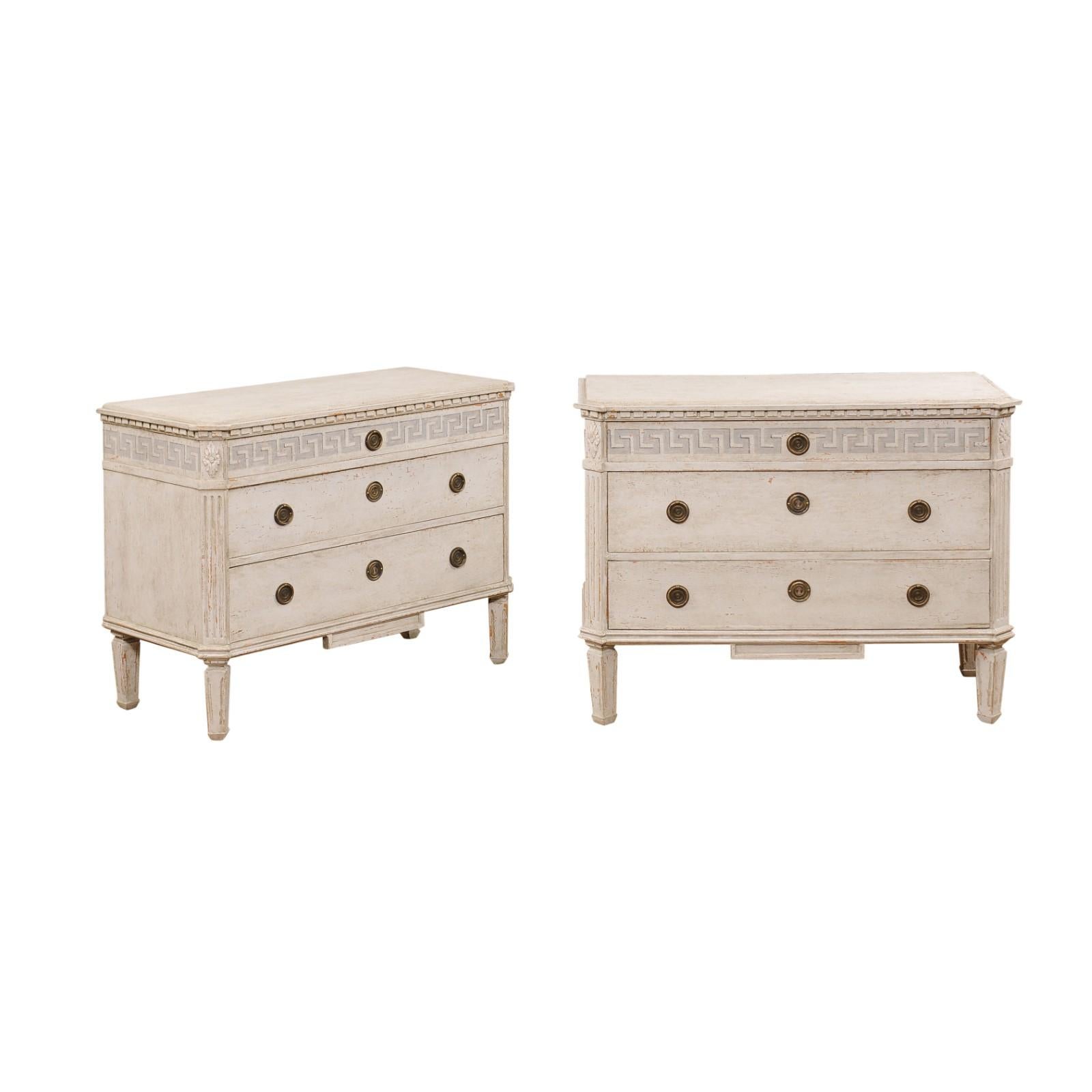 A pair of Swedish Gustavian style painted wood chests from the late 19th century with three drawers, Greek Key frieze, carved rosettes and nicely distressed finish. Created in Sweden during the last quarter of the 19th century, this pair of