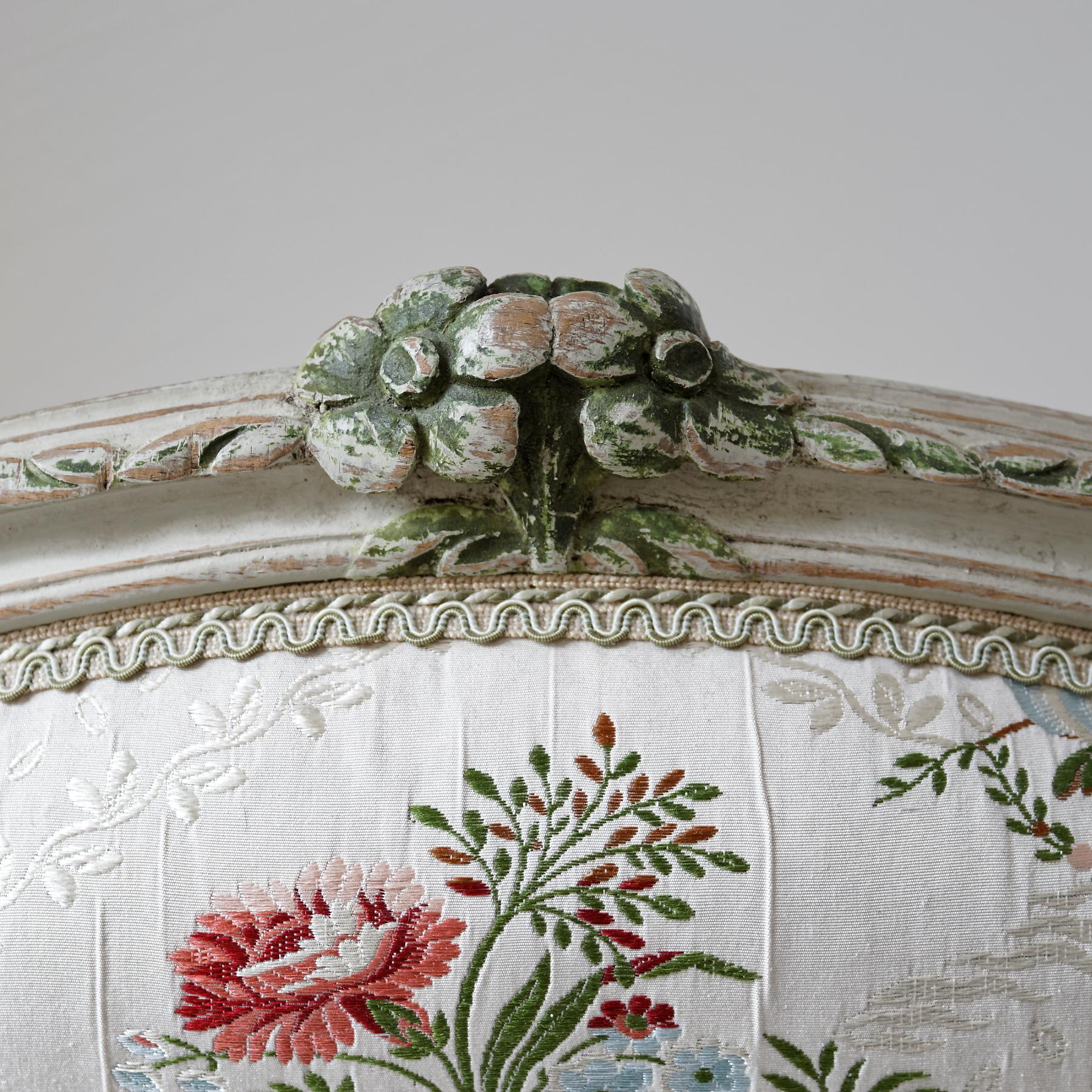 A large and comfortable pair of white and green painted Rococo fauteuils (Fauteuil à la Reine), each with a cartouche-shaped back, the padded arms and seat covered in white floral silk, the chanelled cresting and seat rail centred by floral sprays,