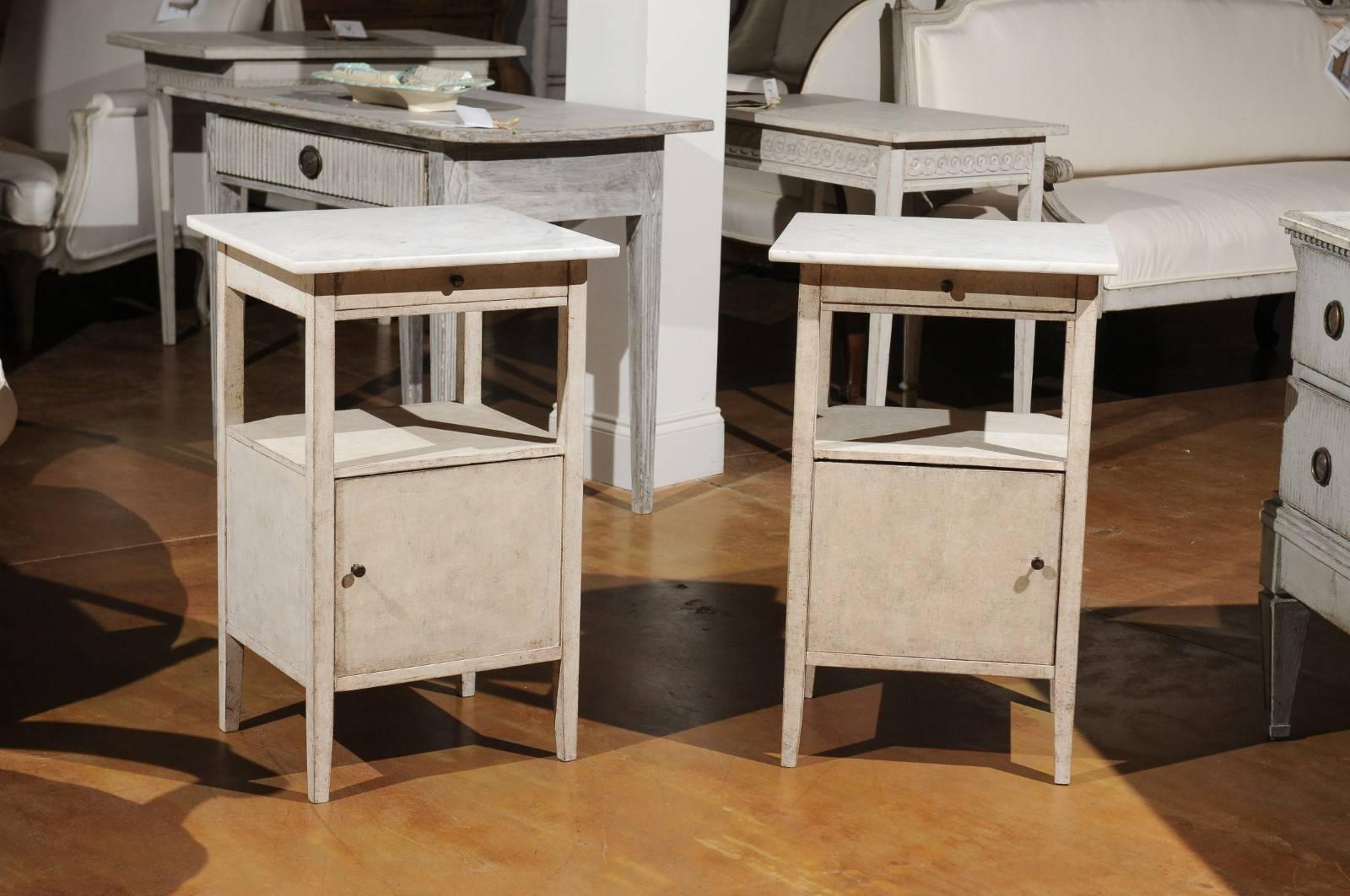 A pair of Swedish painted wood bedside tables from the early 20th century with white veined marble tops, single drawers, open shelved and lower doors. Each of this pair of Swedish beside tables features a rectangular white marble top, overhanging a