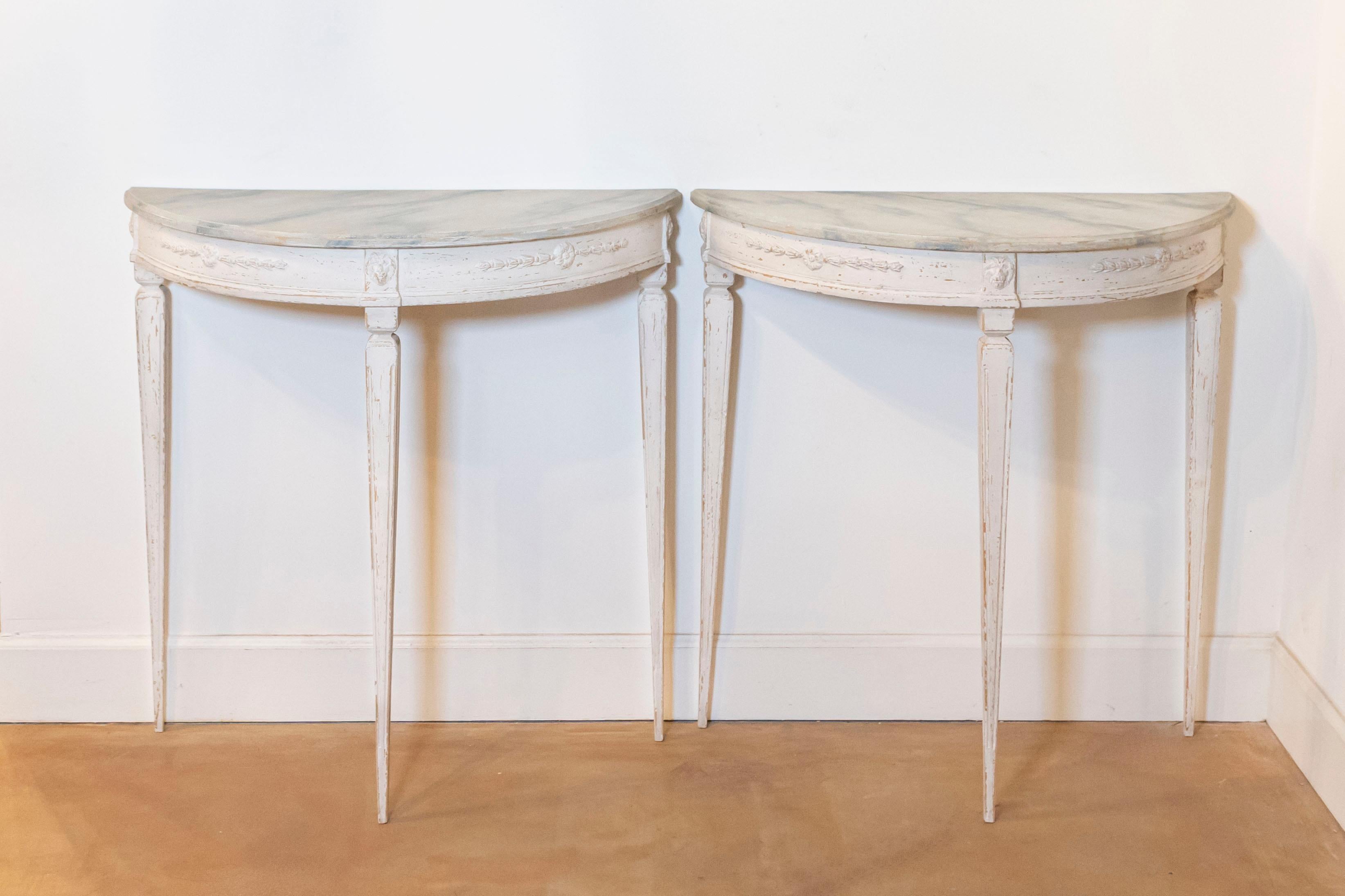 A pair of Swedish Gustavian style painted wood console tables from the early 20th century, with marbleized tops, carved aprons and tapered legs. Created in Sweden during the first quarter of the 20th century, each of this pair of console tables