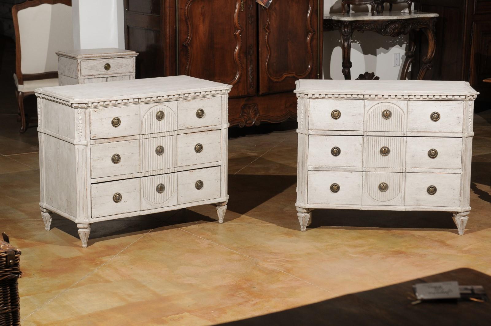 A pair of Swedish Gustavian style painted wood chests from the 20th century, with dentil molding, reeded accents and canted posts. Born in Sweden during the 20th century, each of this pair of painted chests features a rectangular top with canted