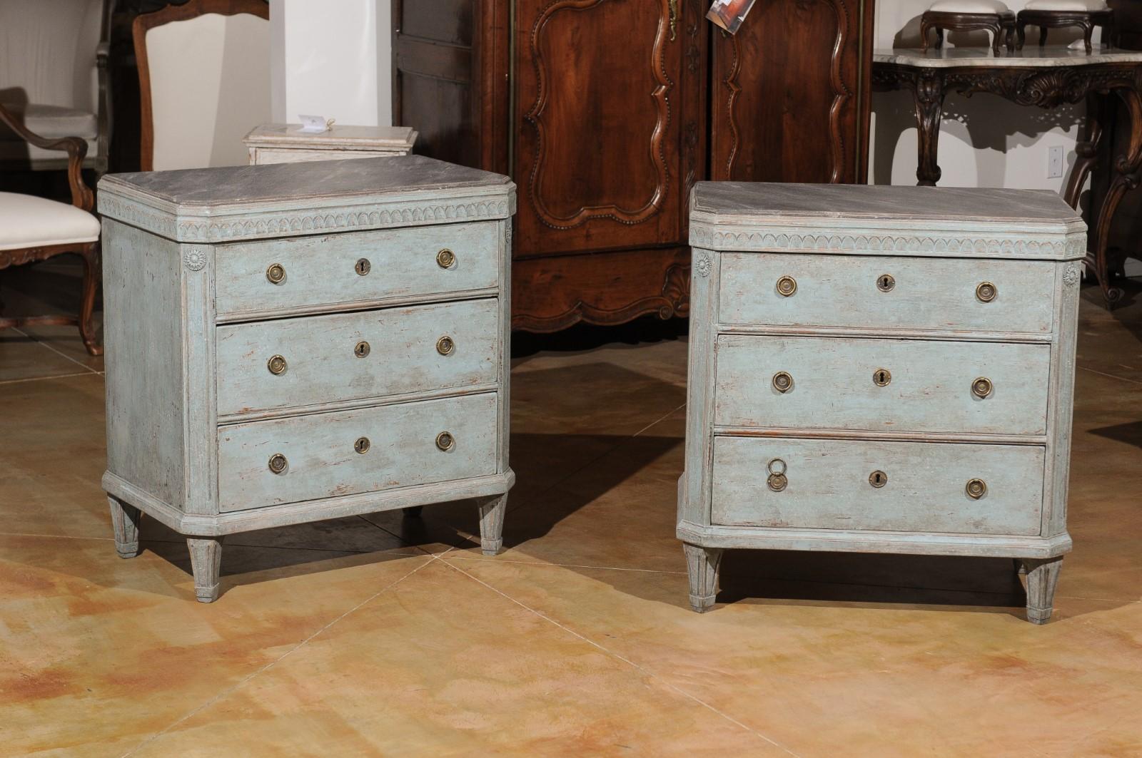 A pair of Swedish Gustavian style painted wood three-drawer chests from the 19th century, with carved waterleaf motifs, rosettes and faux-marble tops. Born in Sweden during the 19th century, each of these Gustavian style painted chests features a