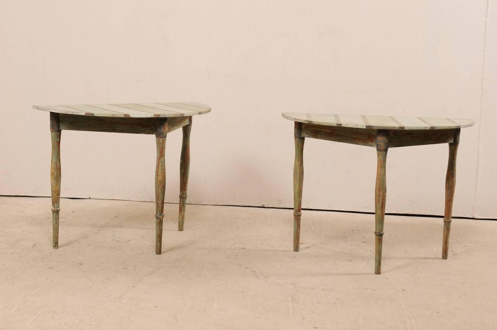 A pair of 19th century Swedish painted wood demilune tables. These antique Swedish demilune tables features a semi-circular top over a triangular shaped apron. Their tops have a custom painted stripe design in sage and blue/grey tones. The apron and