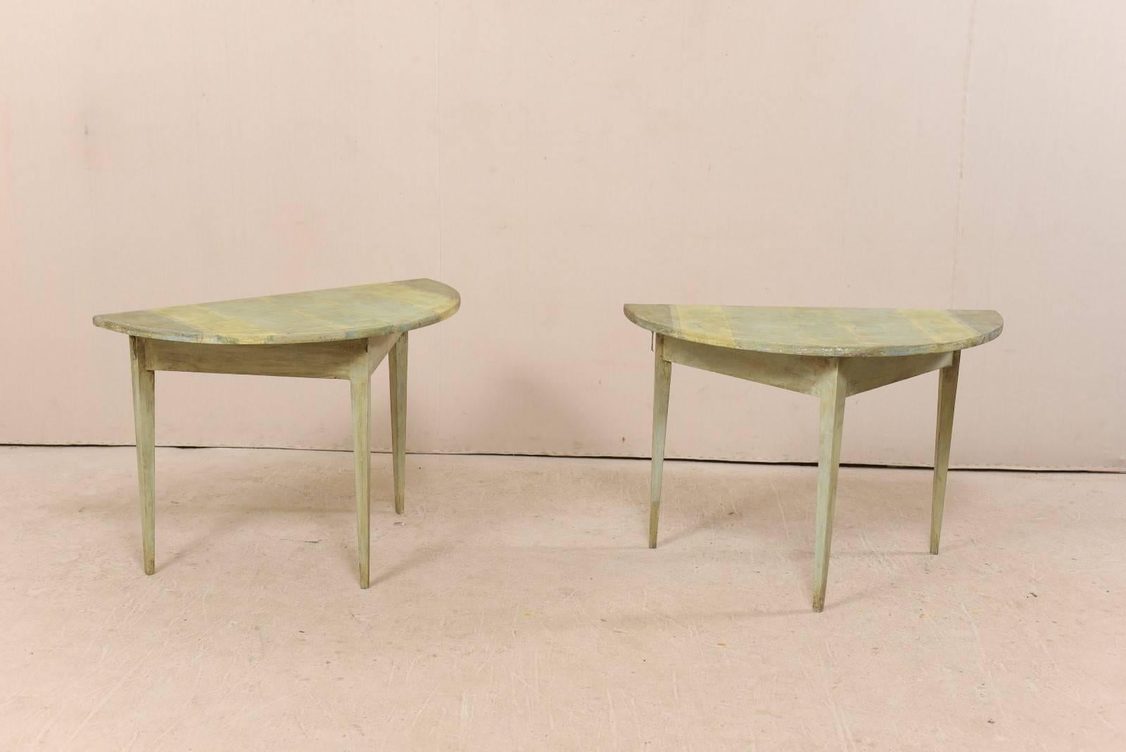 A pair of 19th century Swedish painted wood demilune tables. These antique Swedish demilune tables features a semi-circular top over a triangular shaped apron. Their tops have a painted stripe design in muted shades of celery, taupe and lemon cream.