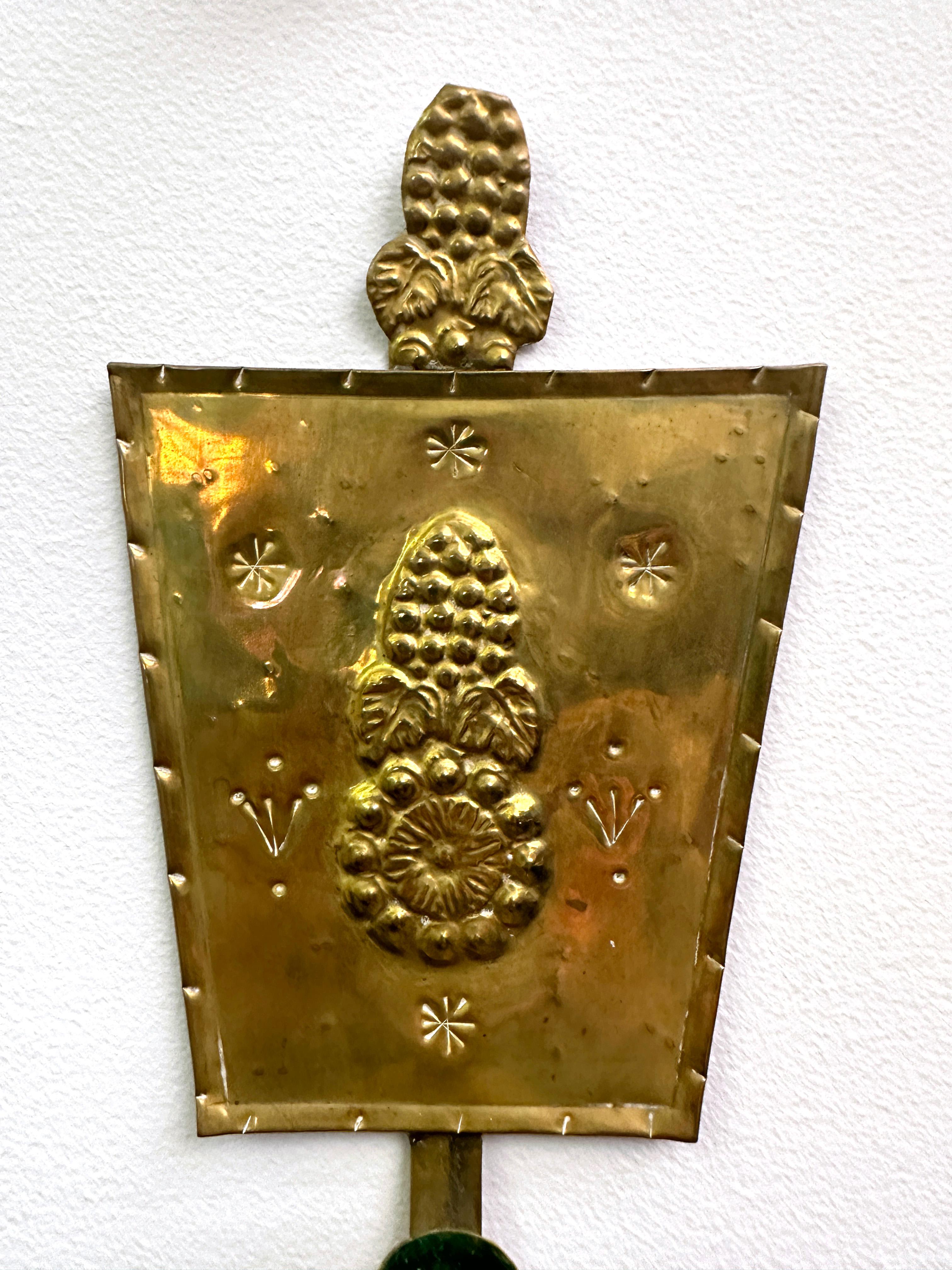 Pair of Swedish Arts & Crafts brass repoussé wall candle sconces. Circa the early 20th Century. Of a trapezoid form with top crown added section. The repoussé is decorated with main oval flower shape, surrounded by smaller carved details. Each