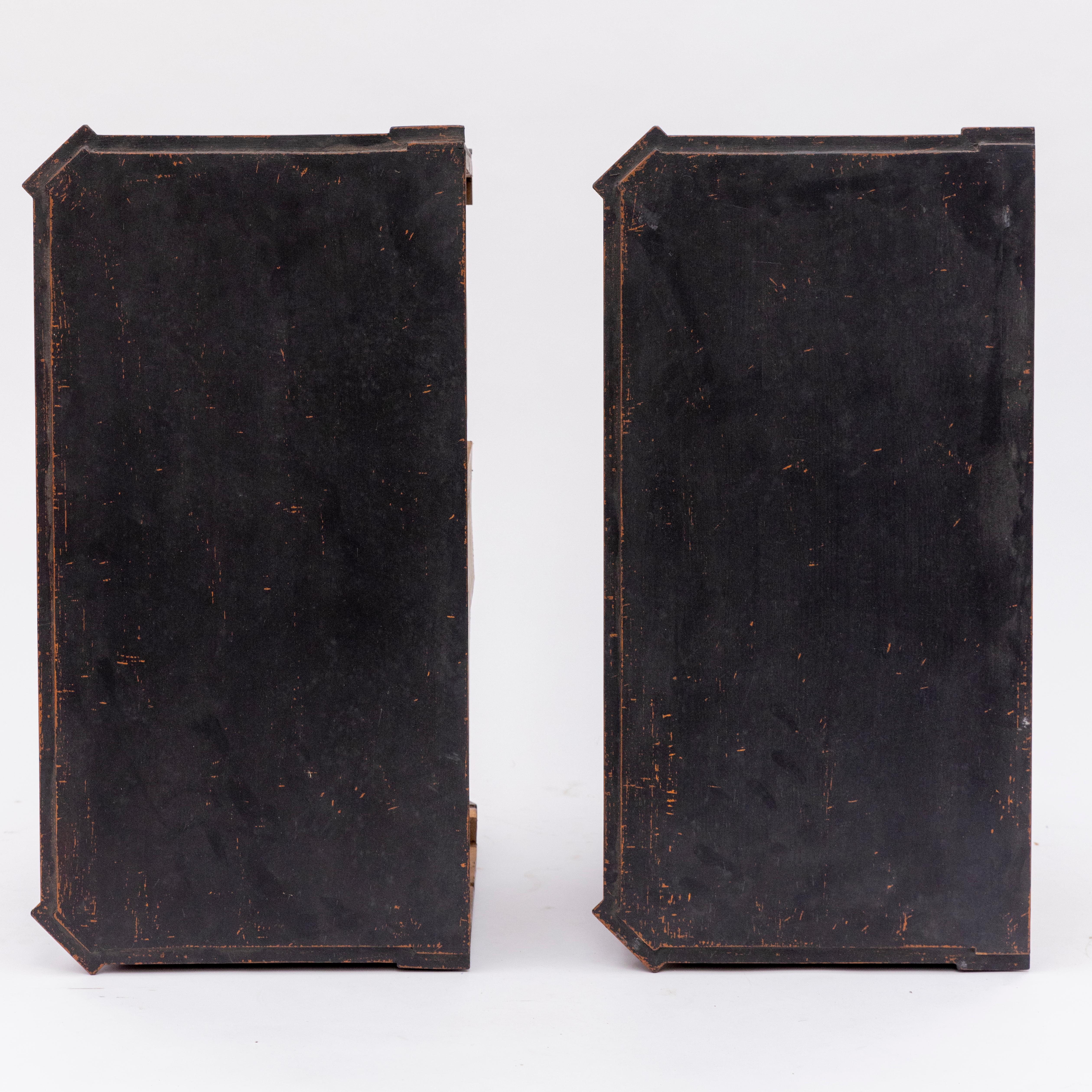 A pair of decorative Gustavian style chests of drawers.
Crafted from black-painted pine with a lovely patina. Each chest has 2 fluted drawer fronts with patinated brass pull handles. The profiled top features dentil moldings. The body has canted