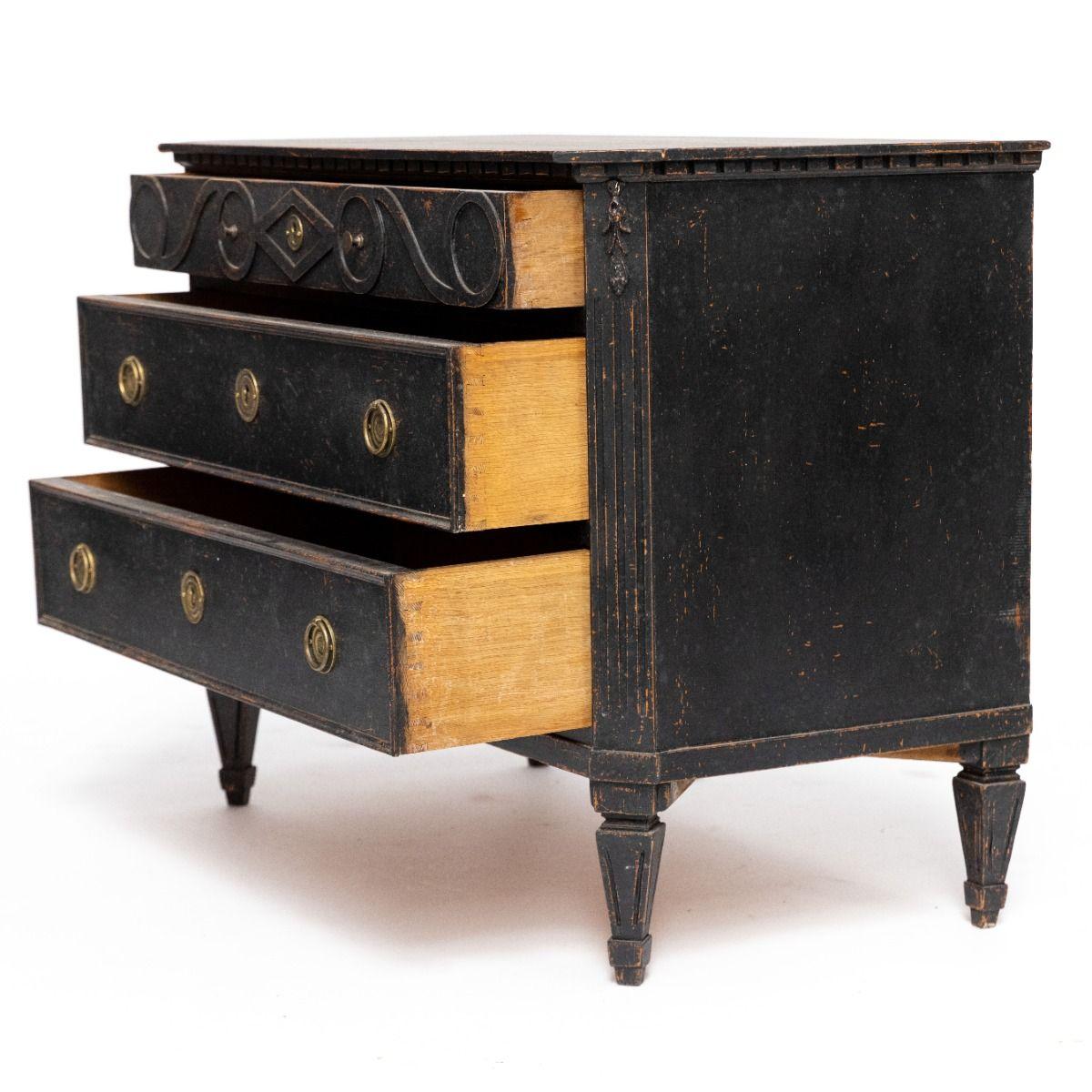 A pair of decorative Gustavian style chests of drawers. 
Crafted from black-painted pine with a lovely patina.
Each chest has 2 drawer fronts with patinated brass pull handles.
The profiled top features dentil moldings. The body has canted corners