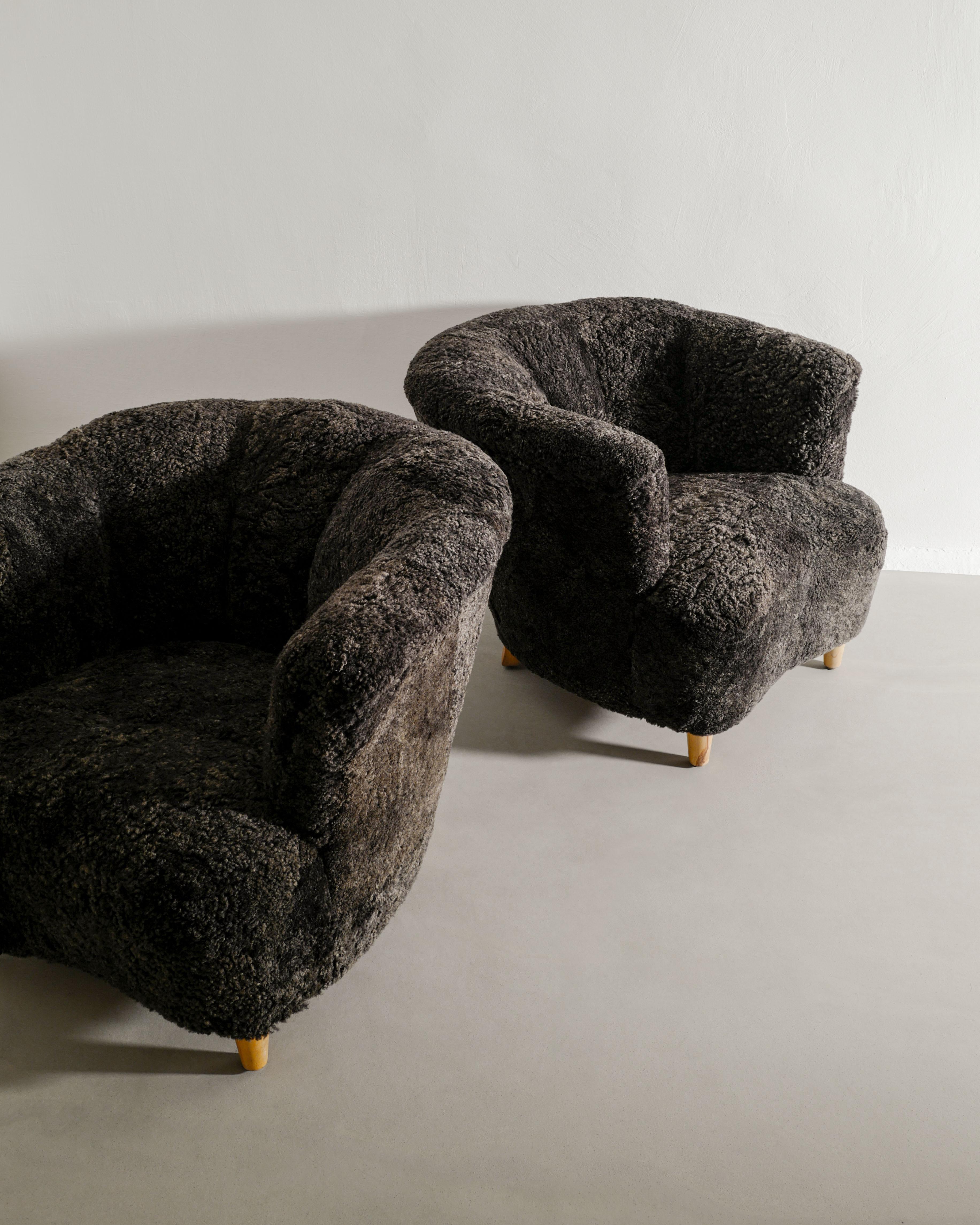 Rare pair of Swedish mid century curved arm easy chairs attributed to Otto Schulz produced in Sweden, 1940s. In good condition and newly reupholstered in a dark charcoal matching sheepskin. 

Dimensions: H: 68 cm / 27