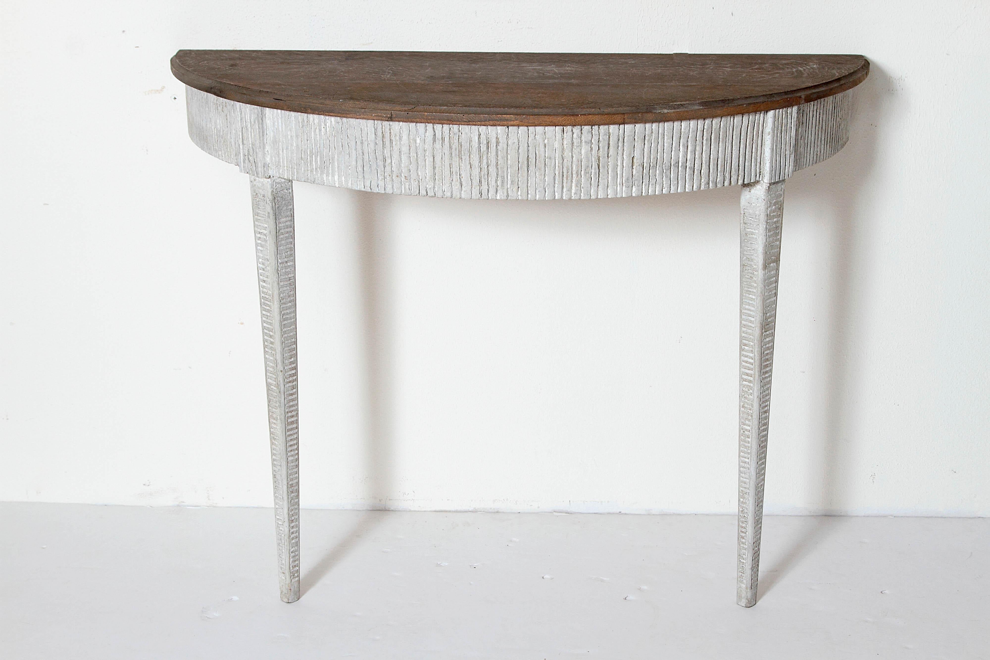 A unique pair of 19th century demilune console tables with grayish white patina and a gray wooden top. The apron is reeded with two well defined joints for the square tapered legs with caved horizontal lines on all four sides.