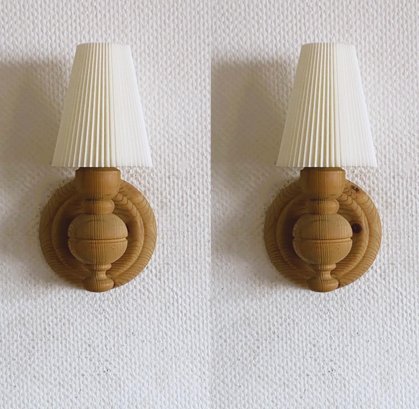 Pair of solid hand-carved pine wood wall sconces designed and produced in Sweden in the 1950s. Clean lines and organic design from the Scandinavian Modern period, with beautiful conical pleated plastic lampshades. Both sconces in very good vintage