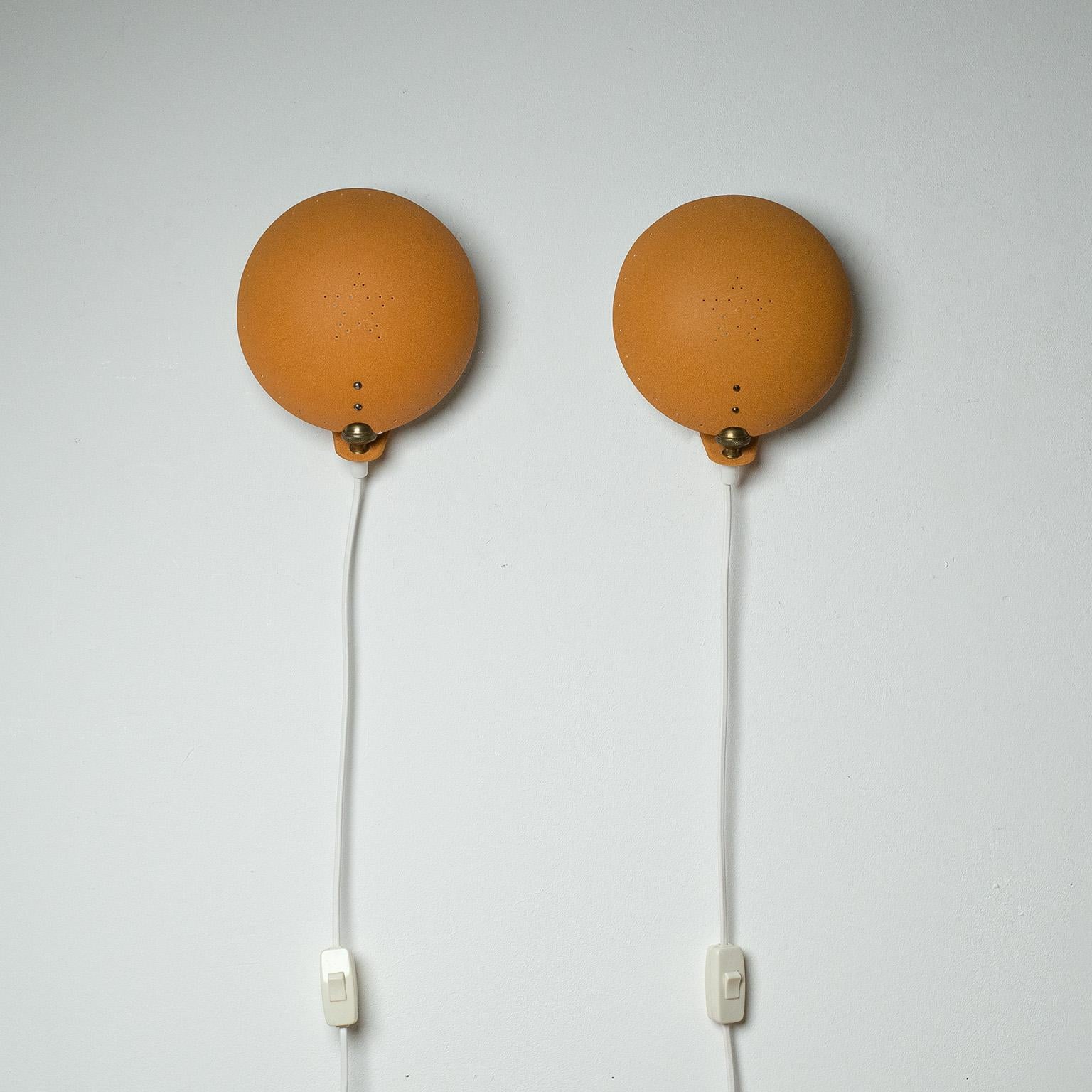 Charming pair of Swedish enameled clam shell sconces from the 1950s. Circular shade enameled in mustard-orange wrinkle paint is pierced around the rim and in the center. Mounted on a joint it has the ability to be tilted and rotated slightly for