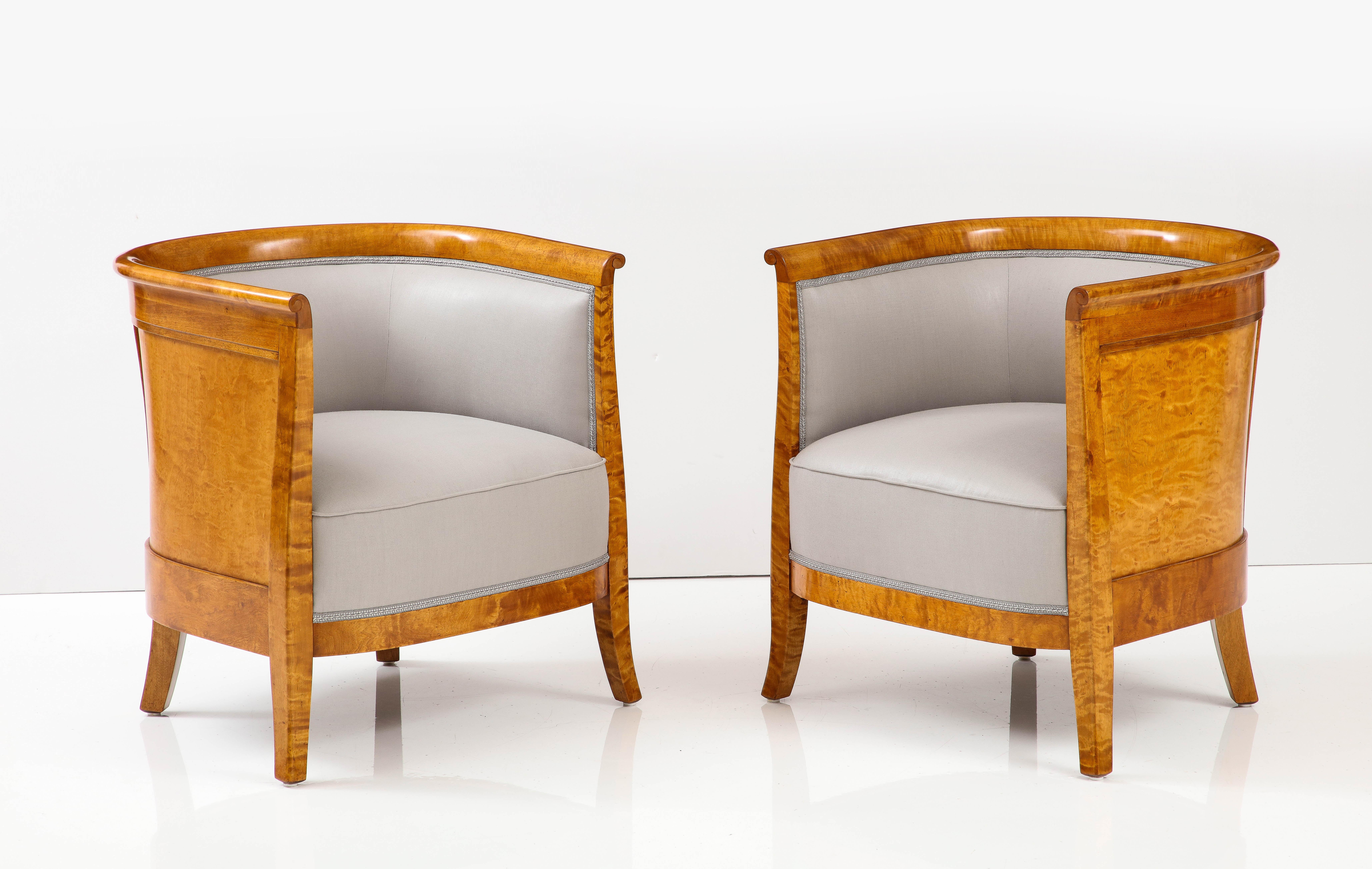 A pair of Swedish Grace flamed birch club chairs, Circa 1930s, each with a partially upholstered curved back and sides, upholstered seat raised on square tapered and slightly out curved legs. The curved backs with birchwood panels. New Rogers &