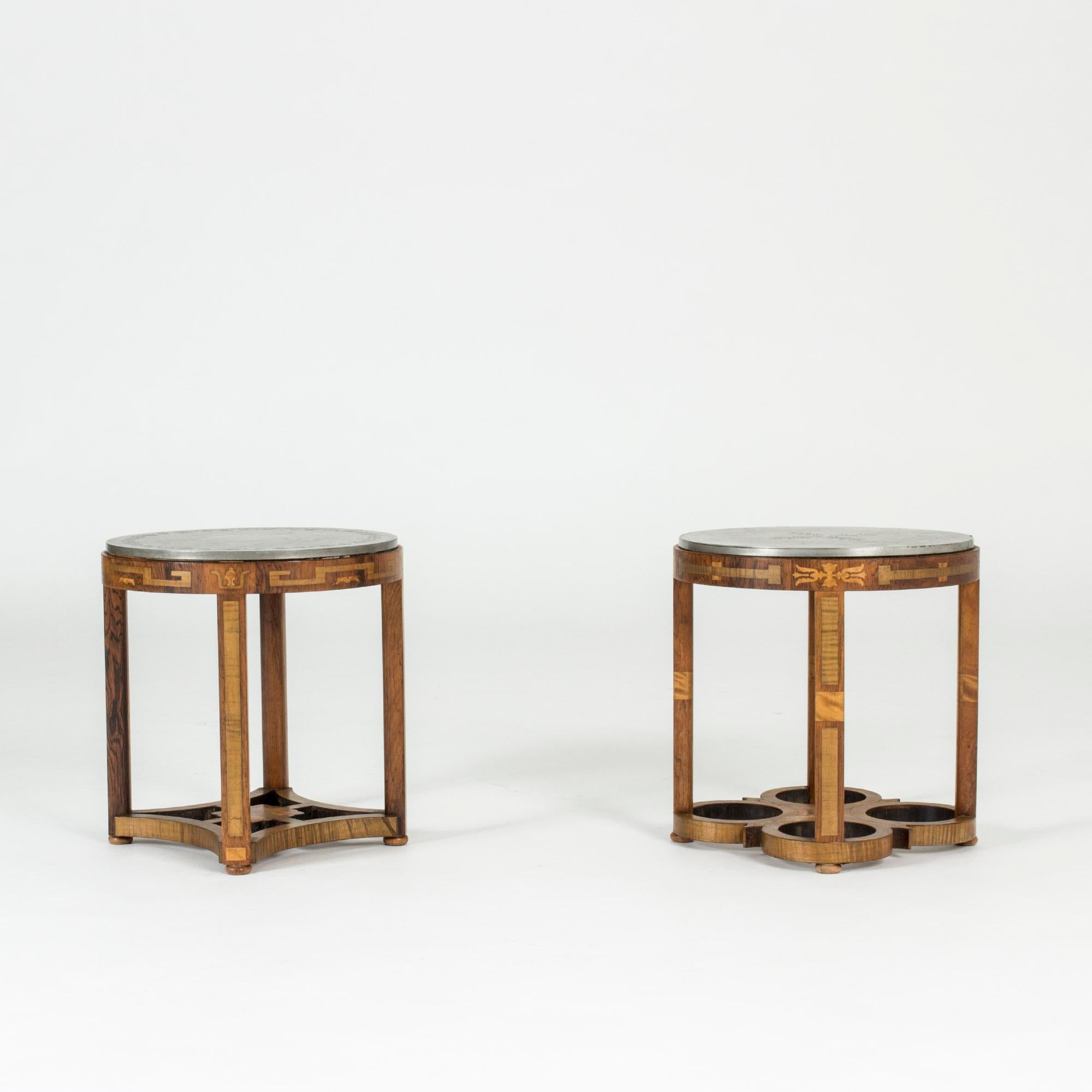 Pair of exquisite side tables from Ystad Tenn from the Swedish Grace period, made in the early 1930s. Beautiful carved wooden bases with inlays. Pewter table tops mounted on top. One with a floral decor in the middle, the other with a classic decor