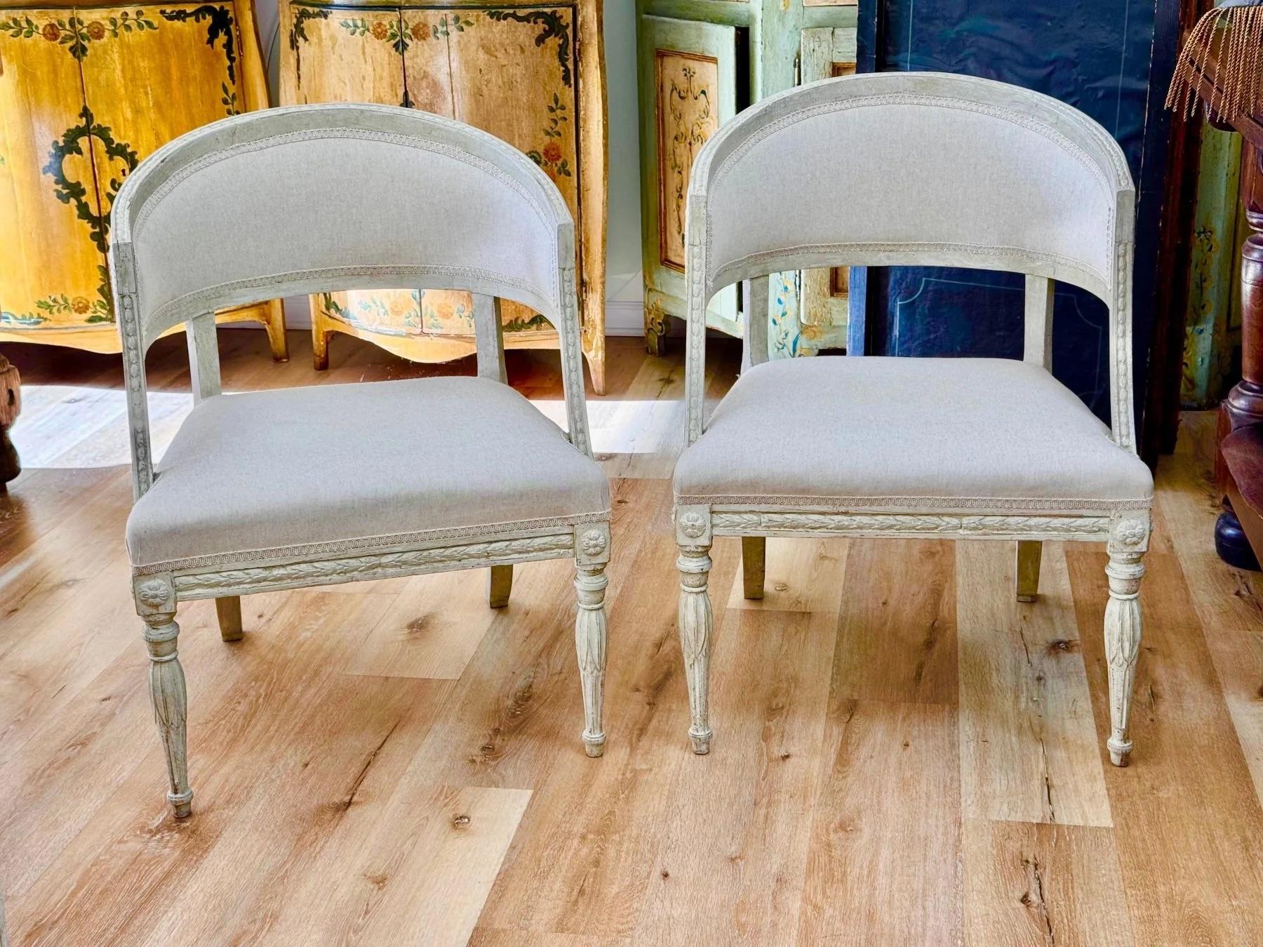 Pair of Swedish Gustavian barrel-back chairs, c. 1800, having floral and foliate detail hand carved frames, seat rails, and in pale, possibly original paint with fine hand carved details and front legs, elegant rear splayed legs and newly recovered