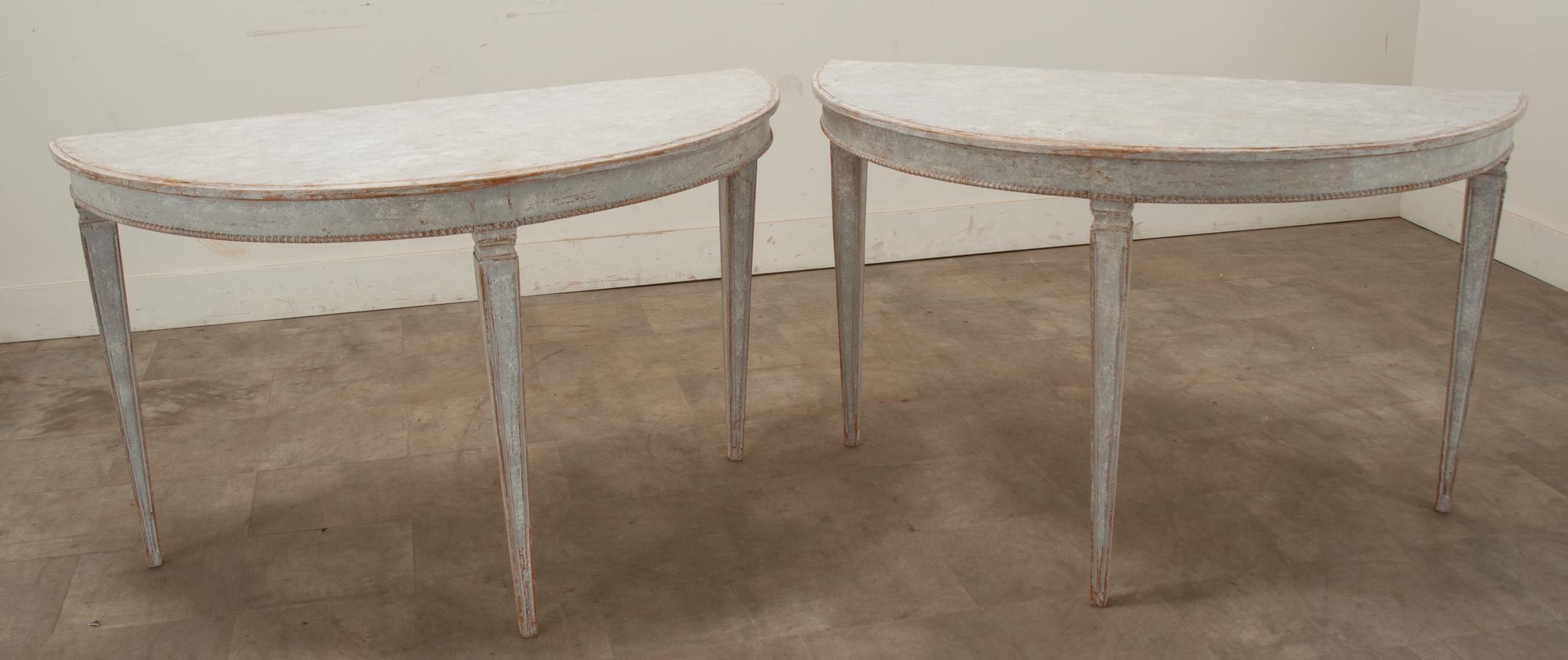 An elegant pair of Swedish Gustavian 18th Century painted demilune consoles. This pair of consoles can be used separately against a wall or they can pull together to create a round center or dining table. Simple in design this pair makes a