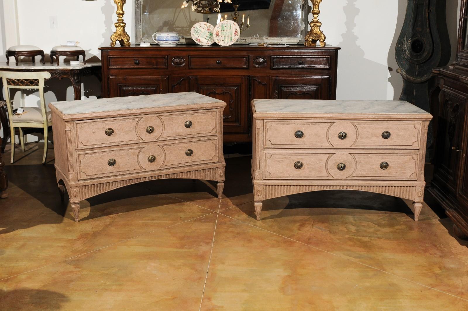 A pair of Swedish Gustavian period two-drawer painted chests from the late 18th century, with marbleized tops, fluted accents and soft pink color. Each of this pair of Swedish Gustavian commodes features a rectangular top with faux-marble inset,