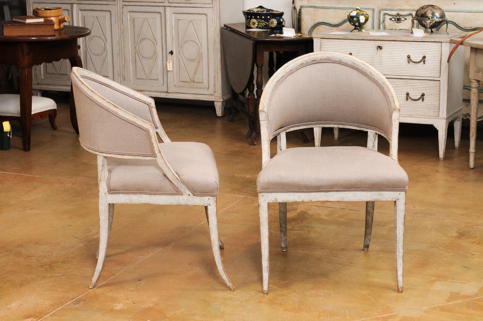 A pair of Swedish Gustavian period painted wood tub chairs circa 1800 with horseshoe backs, saber legs and linen grey/brown upholstery. Experience the understated elegance of this pair of Swedish Gustavian period painted wood tub chairs, dating back