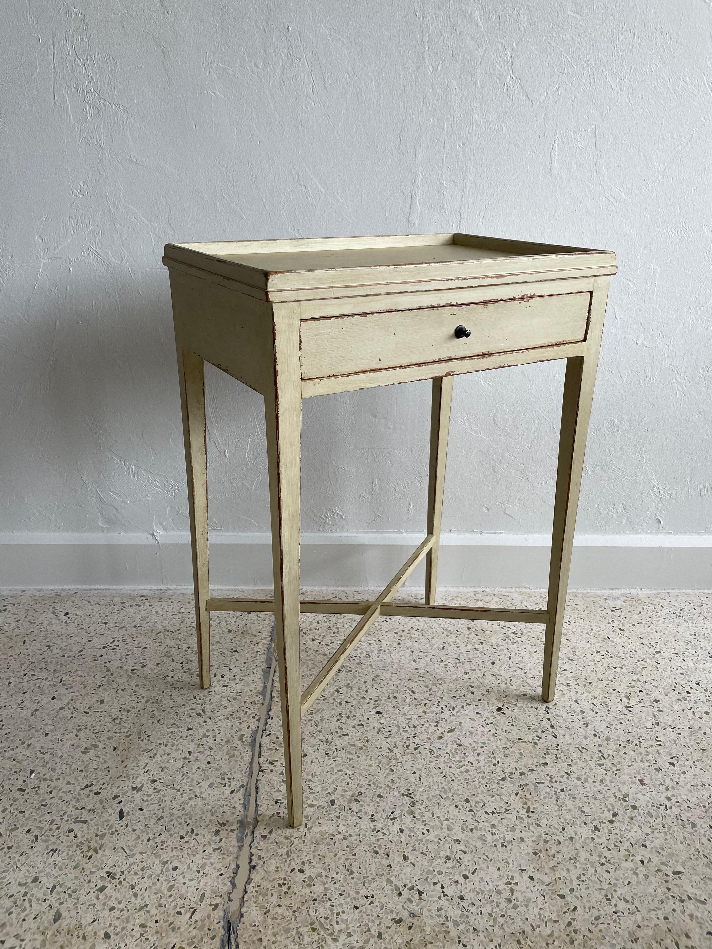 This pair of phenomenal side tables with a single drawer and original dark brass pulls, tapered legs and stretchers - All in a distressed Gustavian style finish in oatmeal tone.