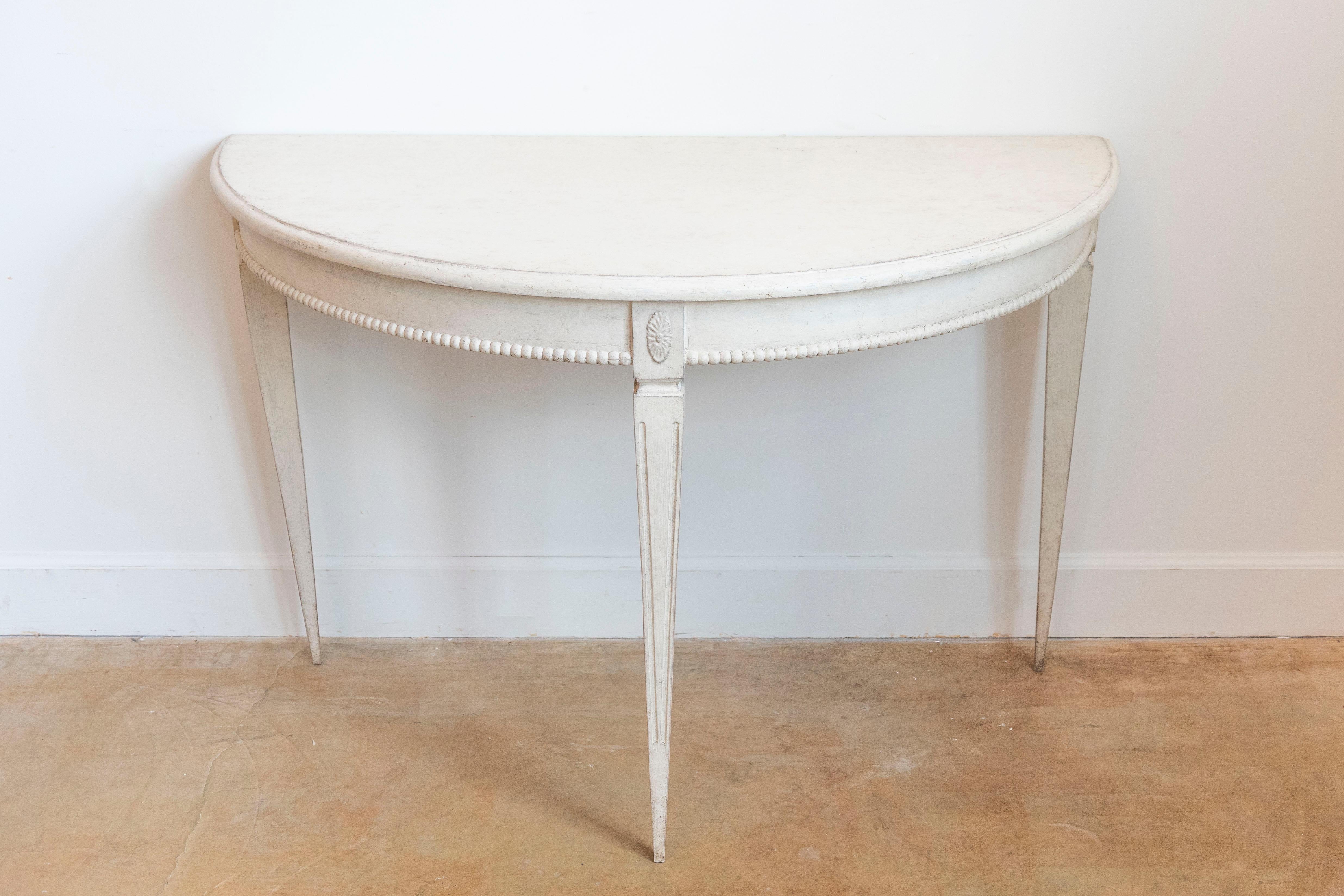 1 LiL - A pair of Swedish Gustavian style painted wood demi-lune console tables from the late 19th century, with carved rosettes, petite beads, tapered legs and fluted accents. Created in Sweden during the last quarter of the 19th century, this pair