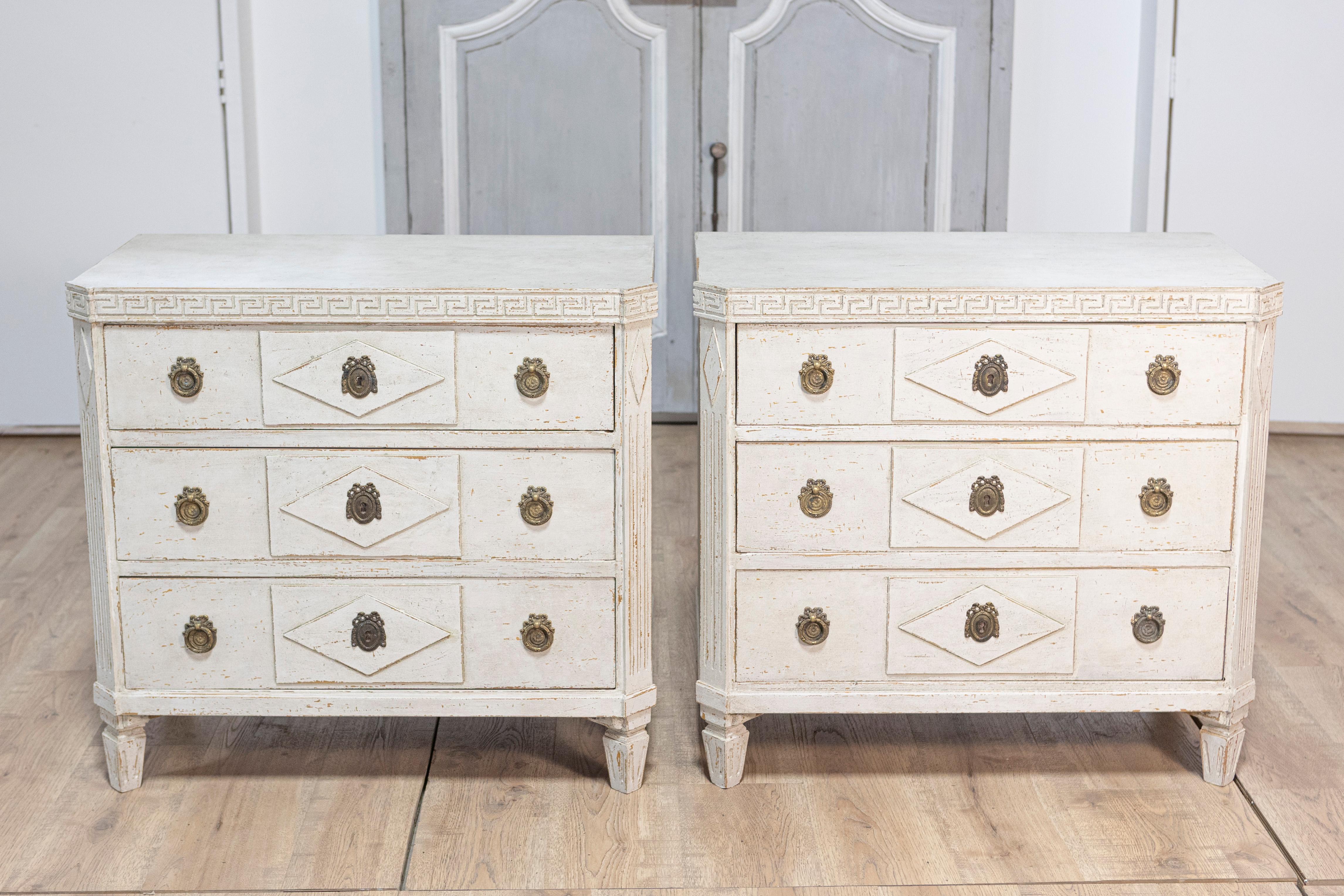 Ein Paar schwedische Kommoden aus bemaltem Holz im Gustavianischen Stil, um 1890, mit drei Schubladen, geschnitztem griechischem Schlüsselfries und Rautenmotiv. Dieses exquisite Paar bemalter Holztruhen im gustavianischen Stil, das um 1890 in