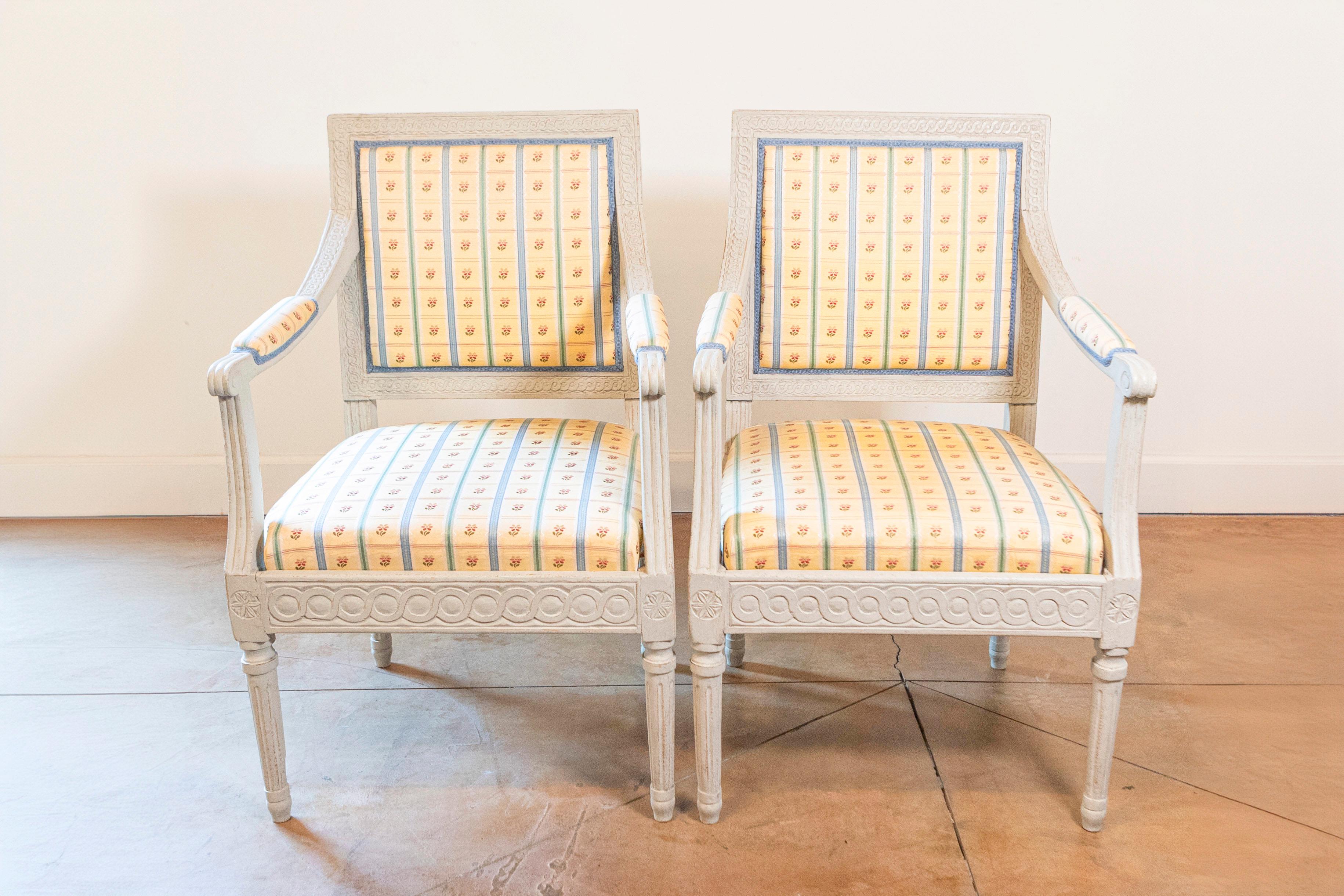 A pair of Swedish Gustavian style painted wood armchairs from the late 19th century, with carved guilloche frieze and upholstery. Created in Sweden during the later years of the 19th century, each of this pair of armchairs features a straight back