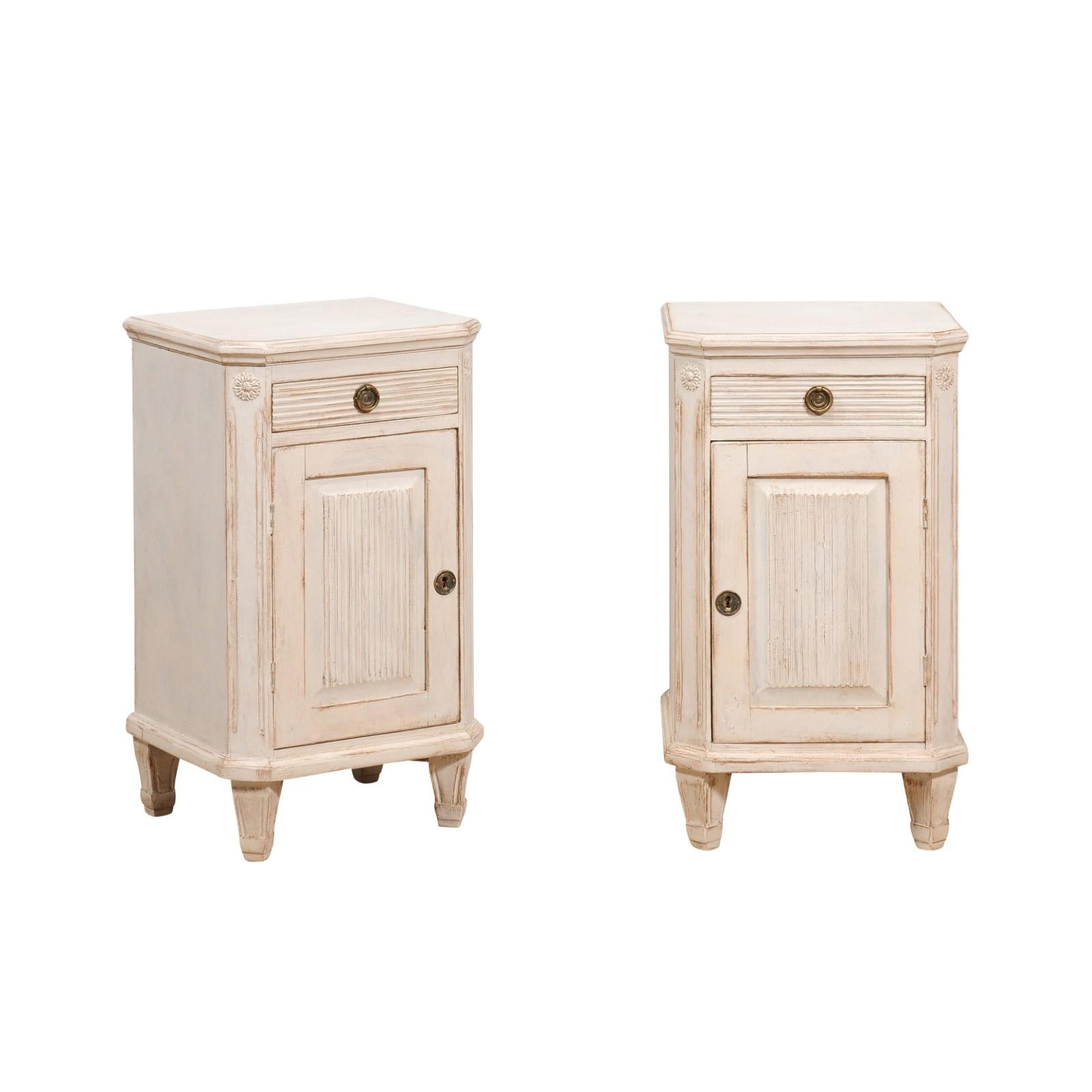 A pair of Swedish Gustavian style bedside tables from the 19th century with off white / light gray painted finish, single drawer and single door. This pair of Swedish Gustavian style bedside tables from the 19th century exudes timeless elegance and
