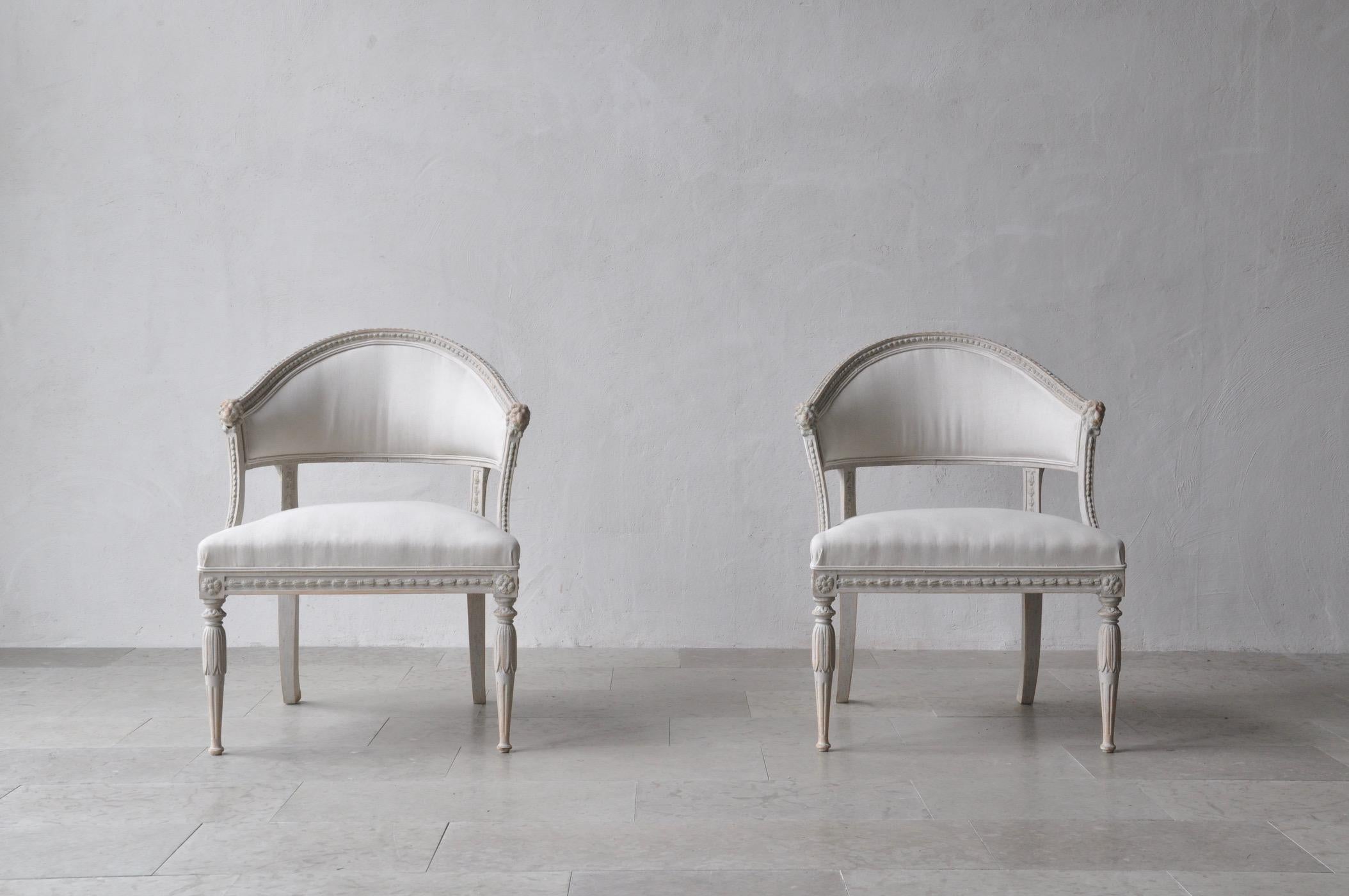 A Swedish Gustavian style pair of antique klismos armchairs. These stunning chairs have barrel backs with cravings of lions' heads. The seat frame features beautiful carving detail and the corner posts are adorned with rosettes. This pair has been